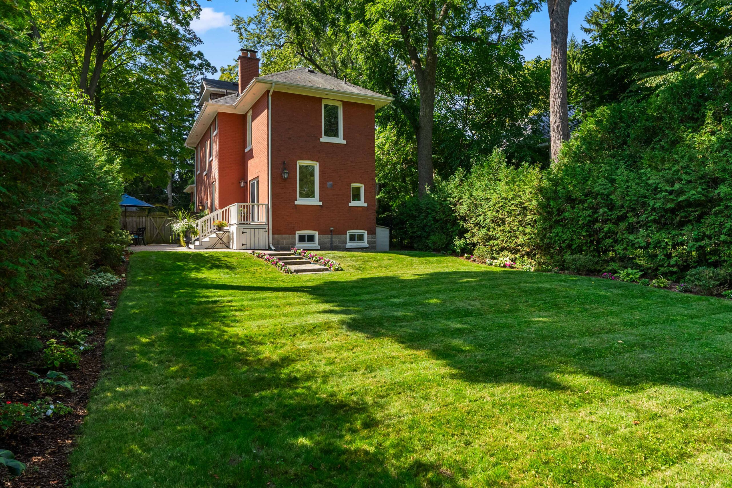 Red brick house surrounded by lush green lawn and trees