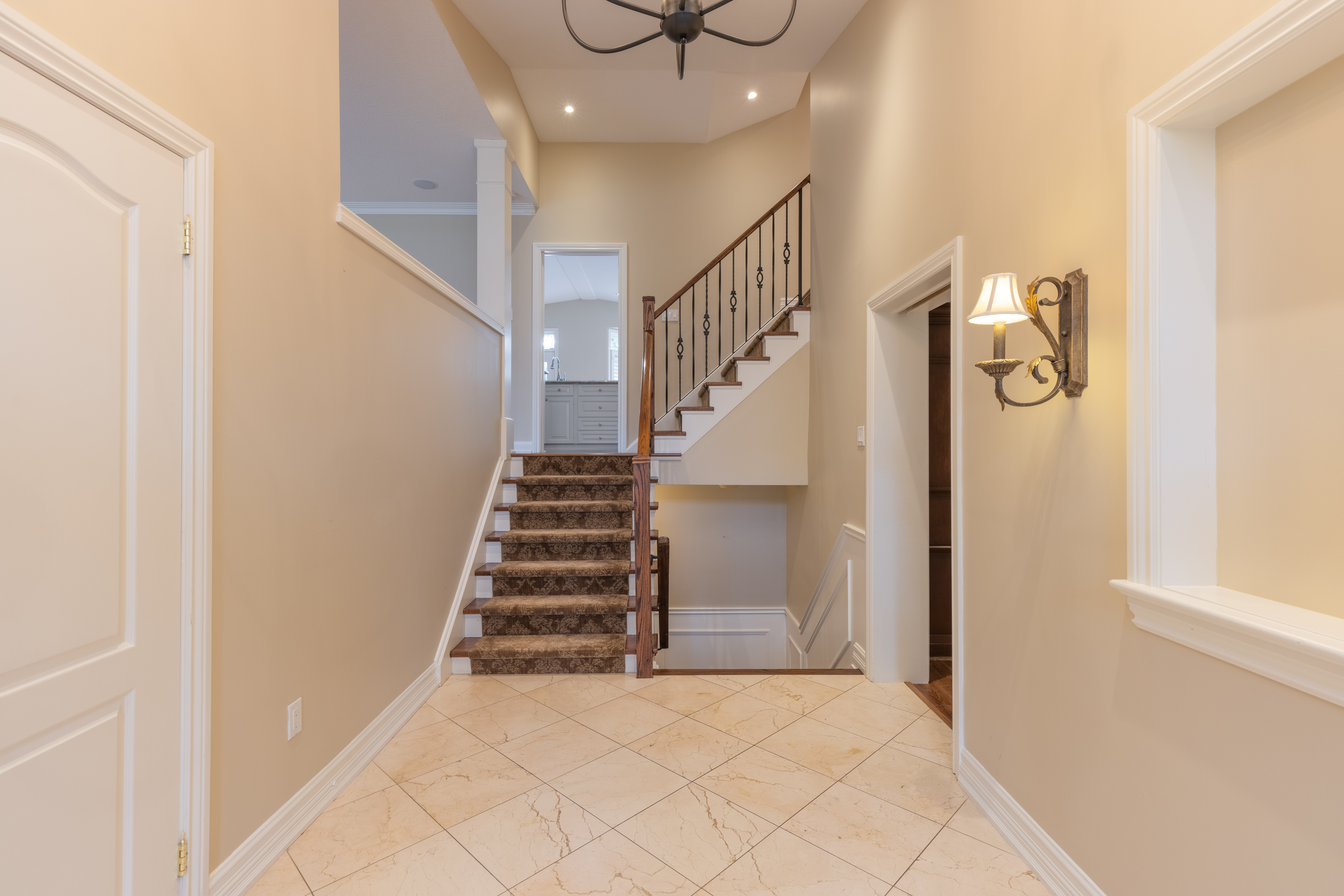 Bright hallway with staircase, light fixtures, and beige walls