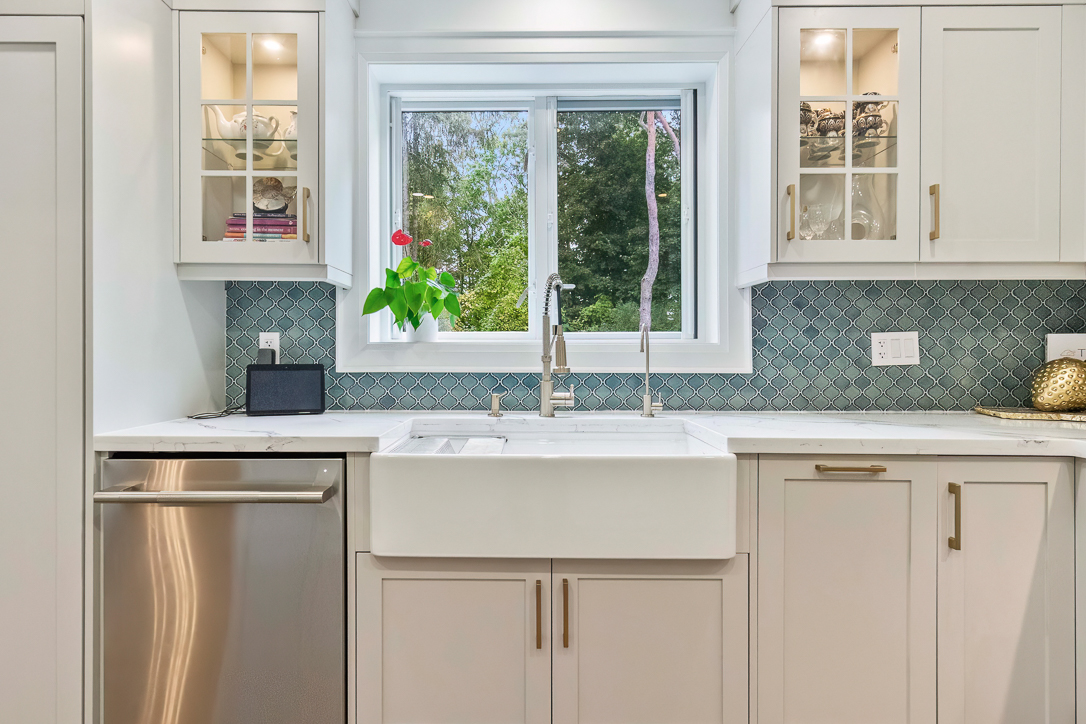 Modern kitchen with a farmhouse sink, green backsplash, and window view.
