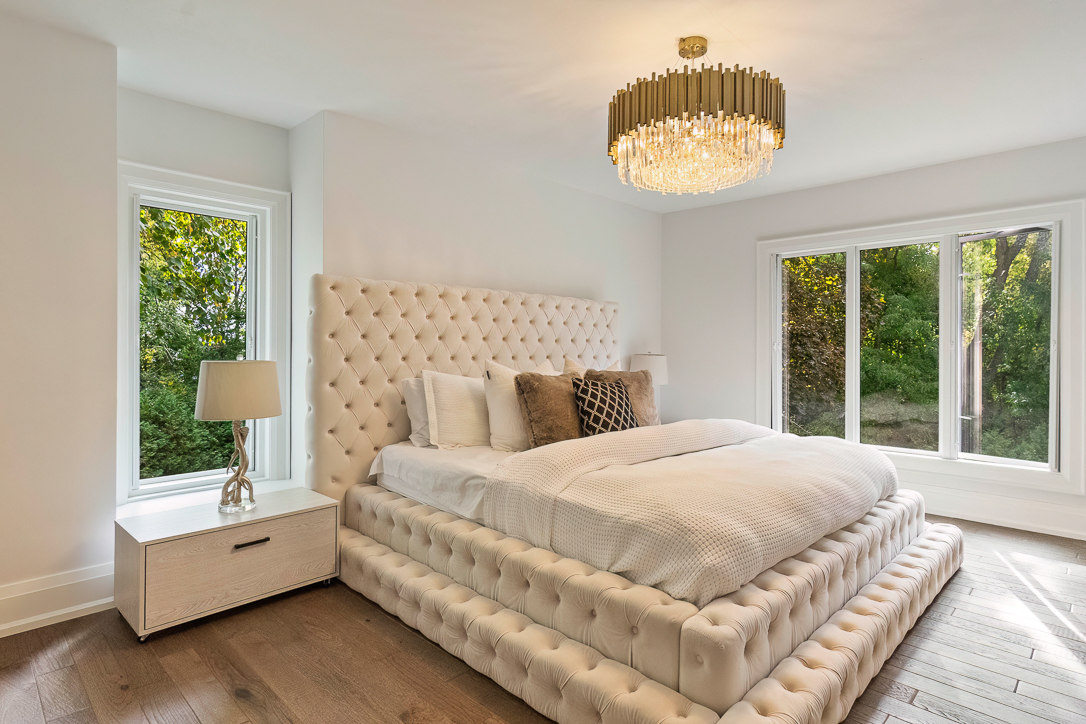 Modern bedroom with a tufted bed, chandelier, and large windows.