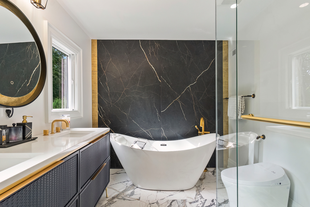 Modern bathroom featuring a freestanding tub, dark marble wall, and gold accents