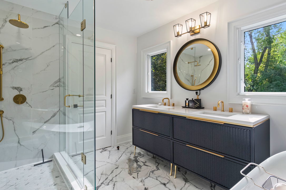 Modern bathroom with marble flooring, gold accents, and a large round mirror