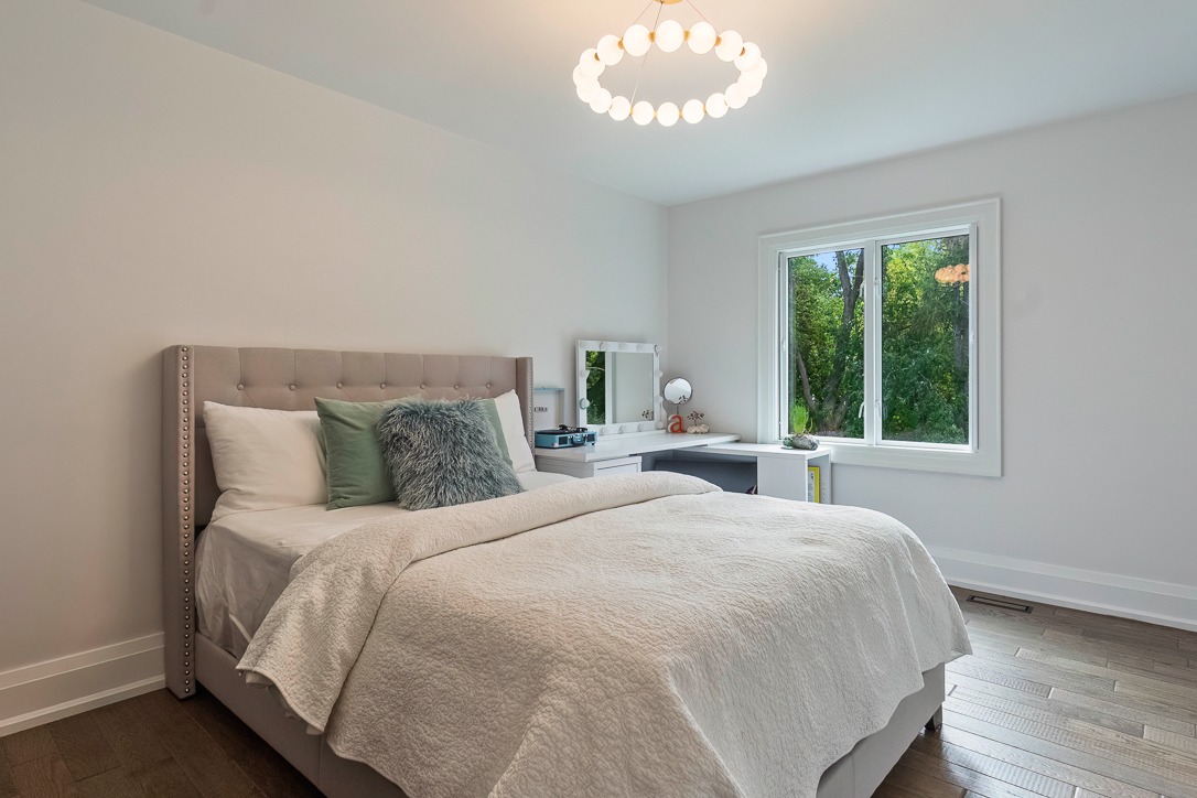 Modern bedroom with a large window, light-colored walls, and stylish chandelier.