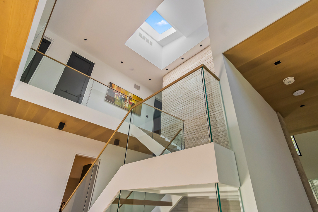 Modern staircase with glass railing and skylight above