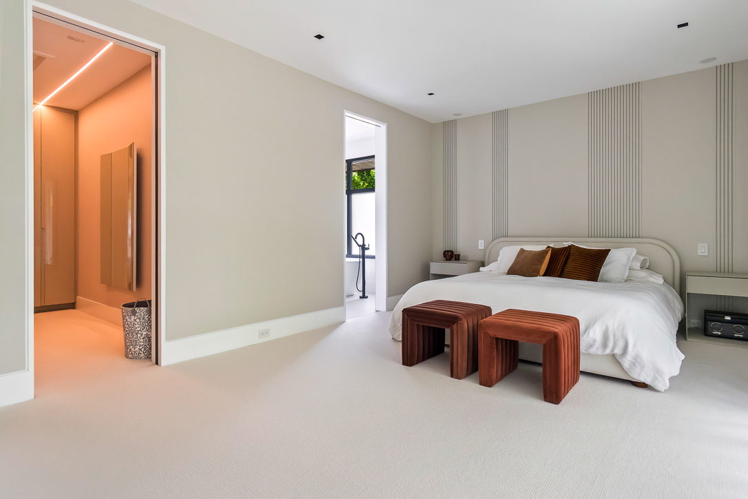 Modern bedroom with a white bed, orange stools, and neutral walls