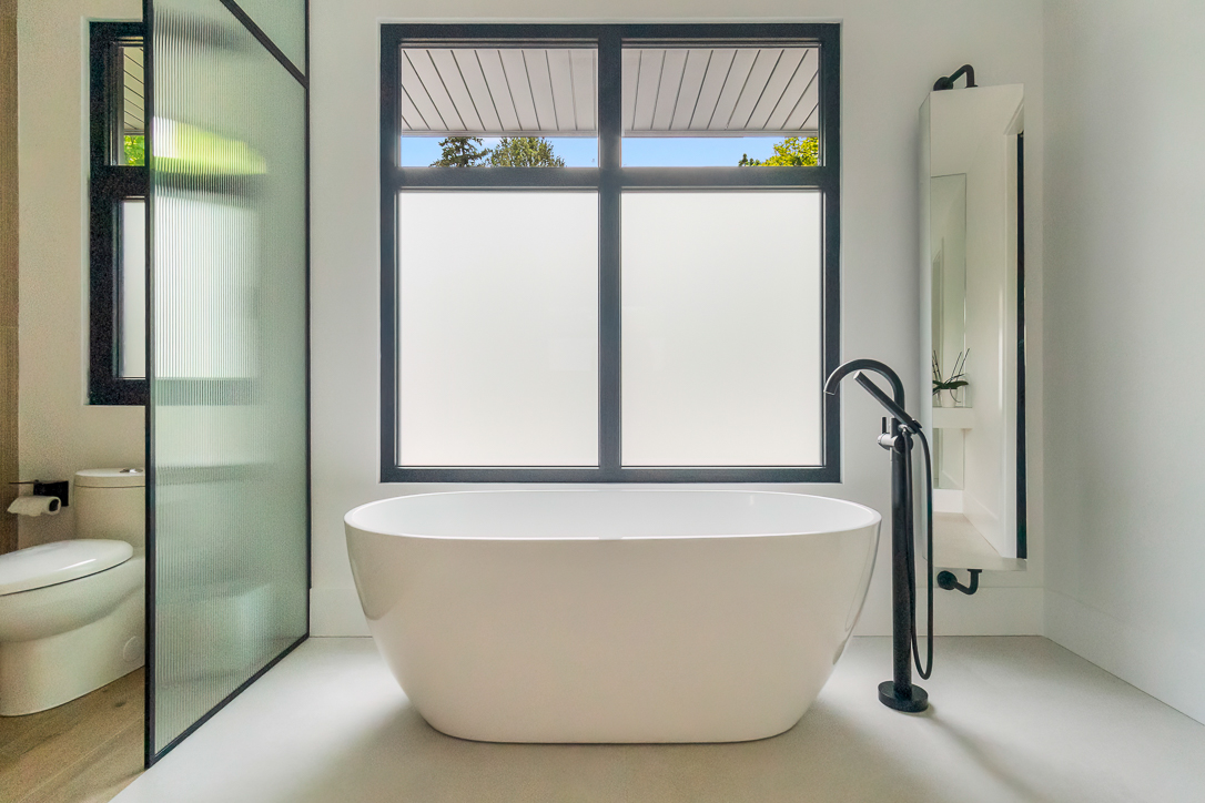 Modern bathroom featuring a freestanding tub and large windows.