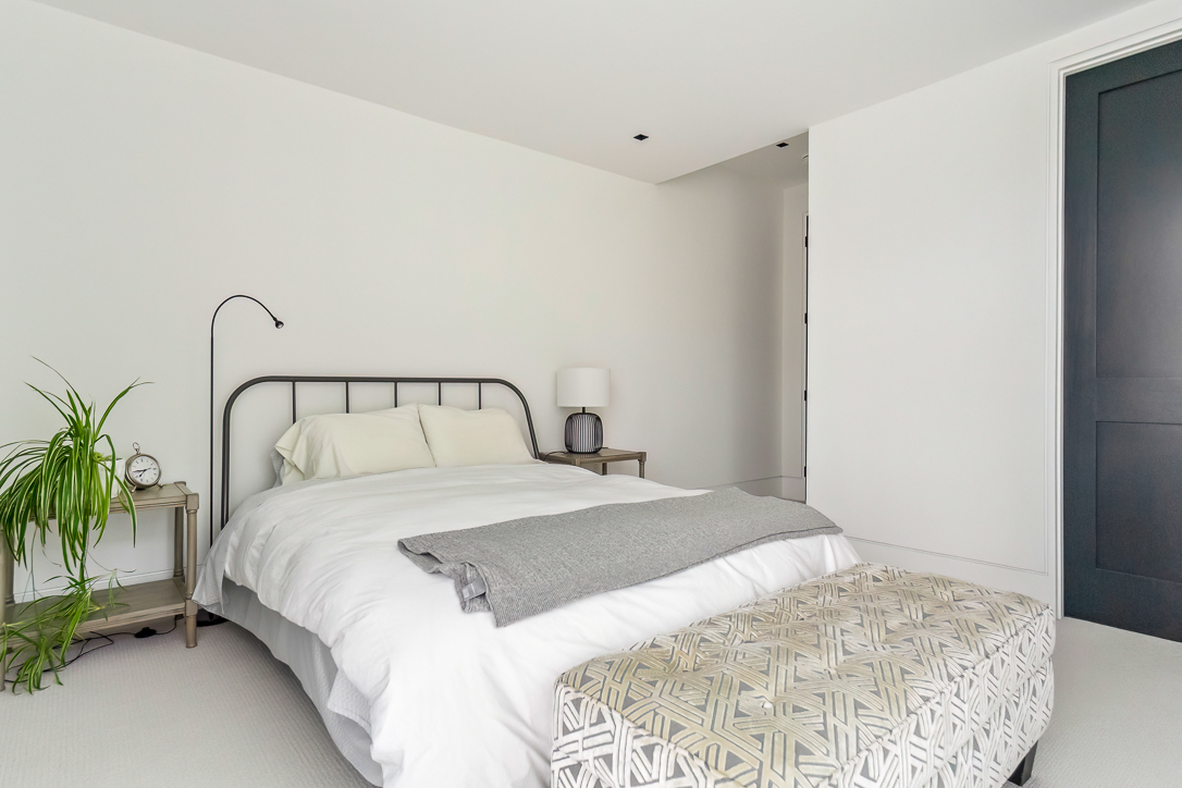 Minimalist bedroom with a bed, nightstands, and a plant.