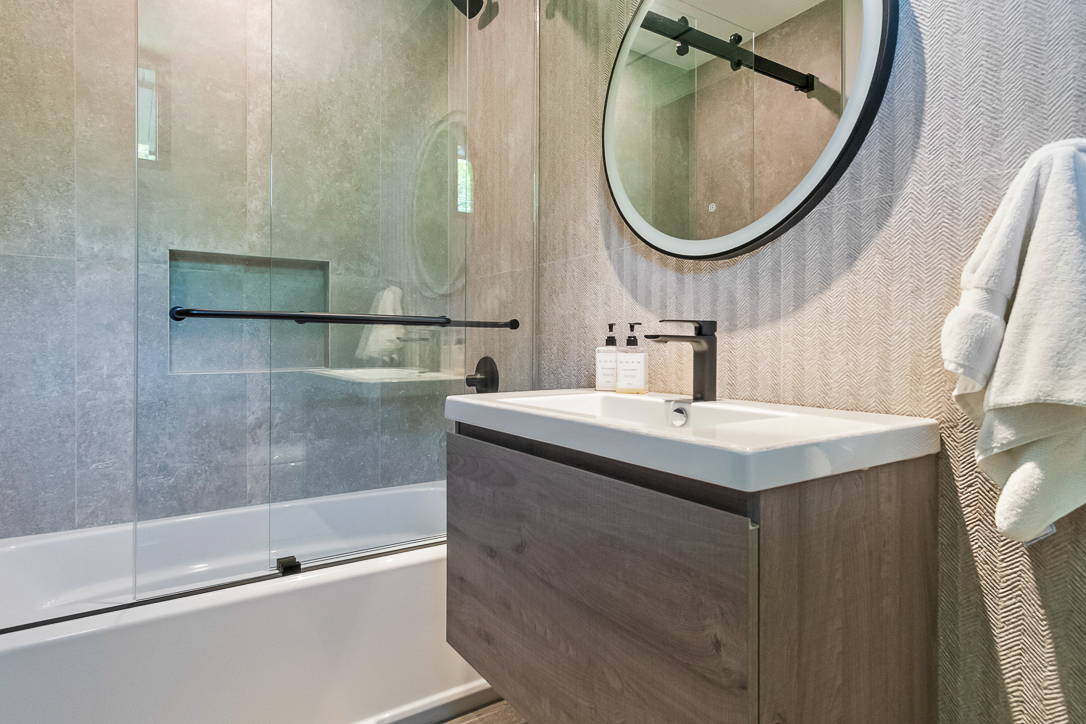 Modern bathroom with a round mirror, wooden vanity, and glass shower enclosure