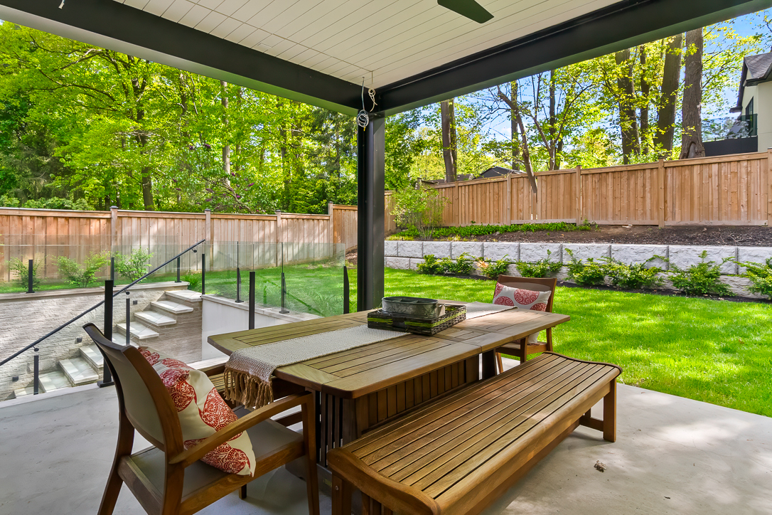 Covered patio with wooden dining table and benches overlooking a green backyard