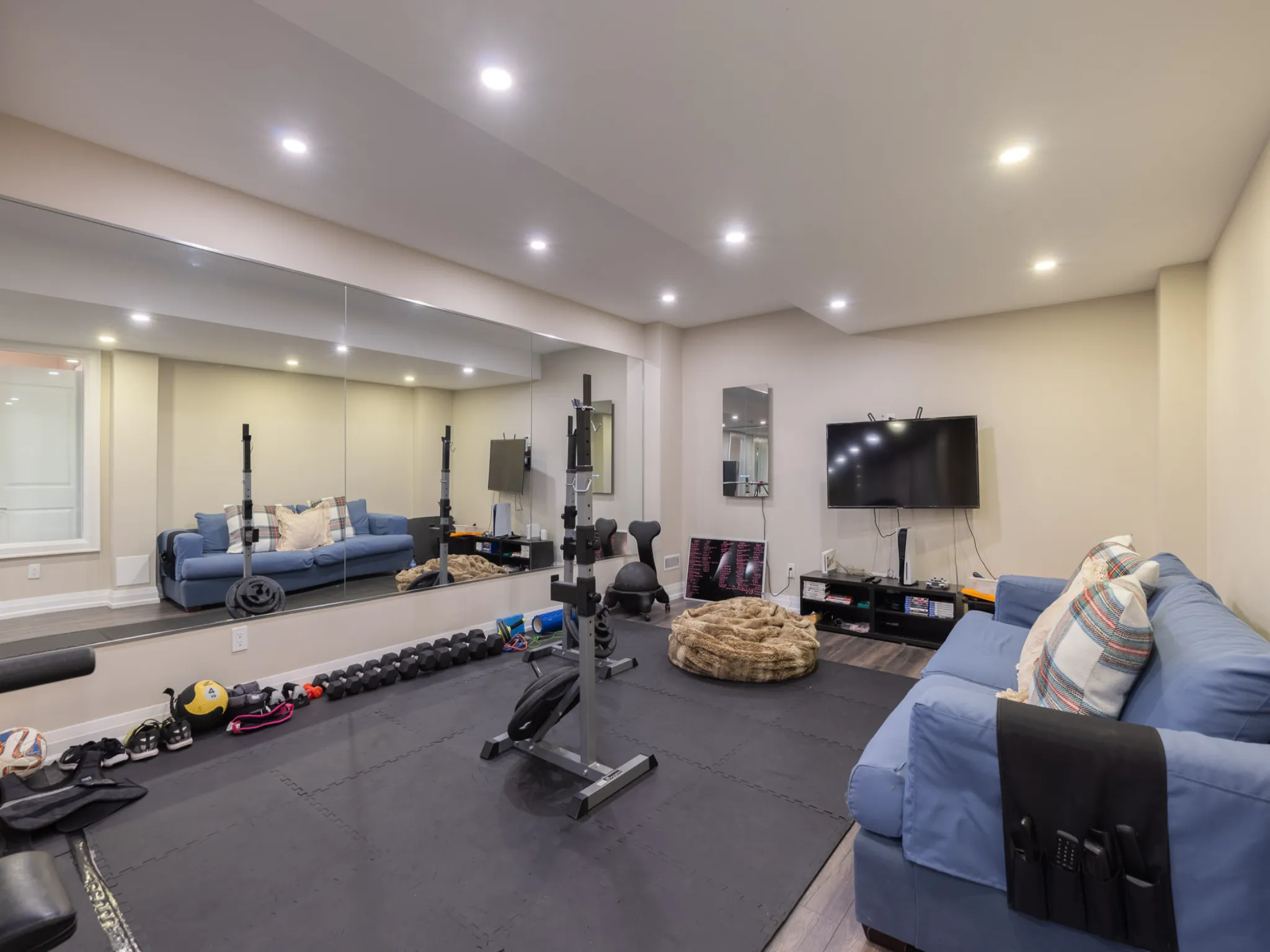 lower level personal gym with big mirror and tv on the wall