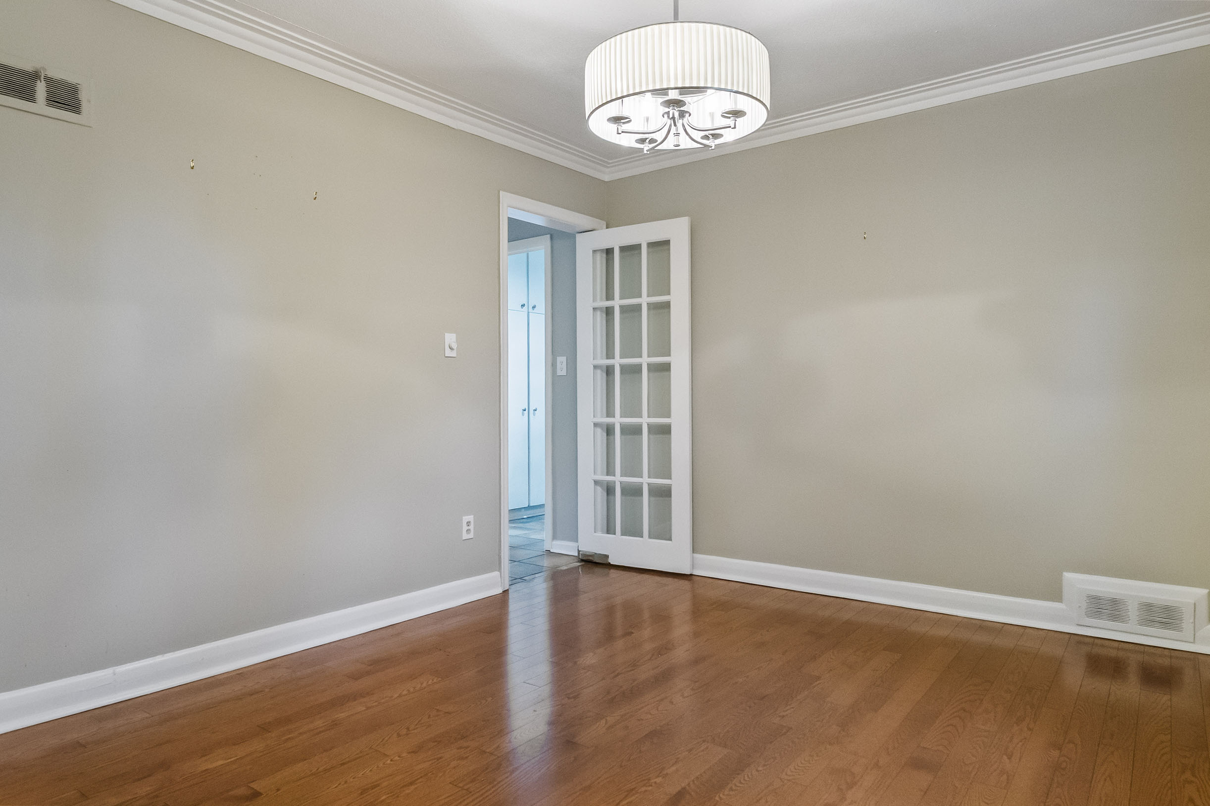 Empty room with hardwood floor and a chandelier, featuring a blue door.