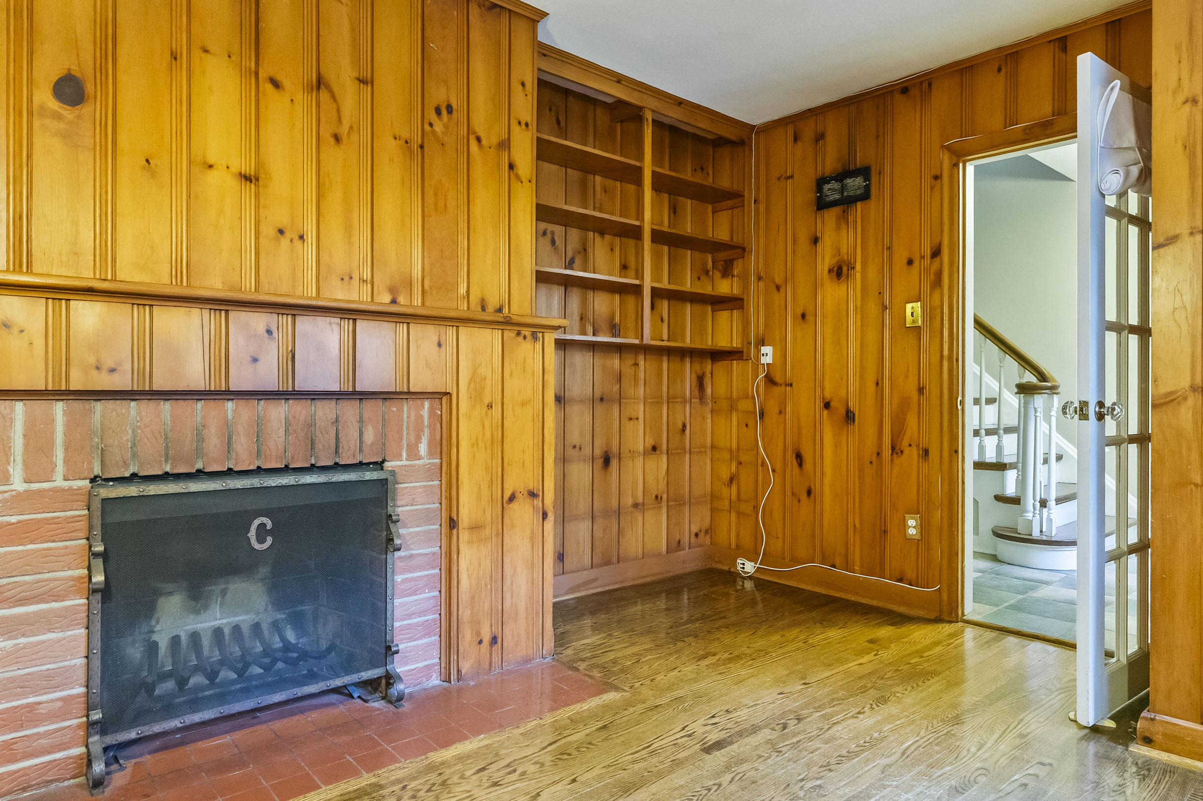 Cozy room with wooden paneling, fireplace, and open doorway to stairs