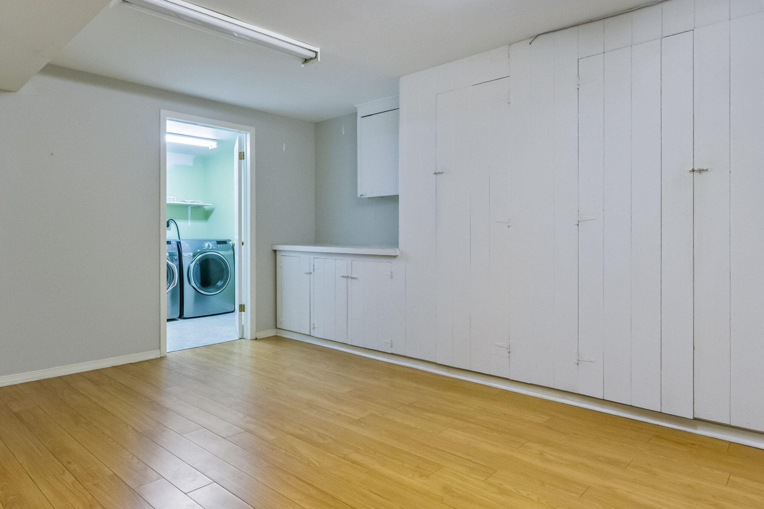 Bright laundry room with wooden flooring and white cabinetry
