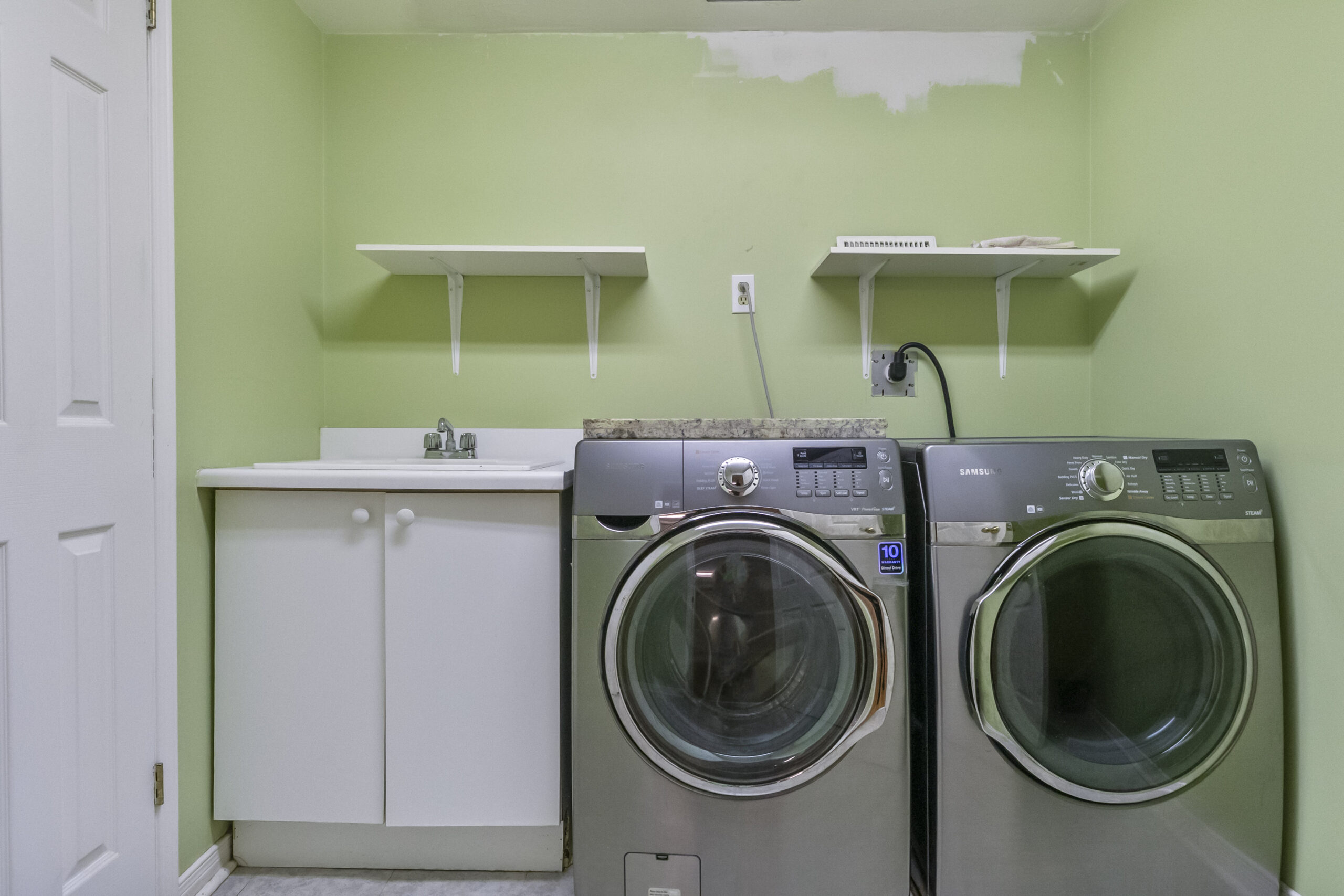 Laundry room with green walls, two washing machines, and white shelves