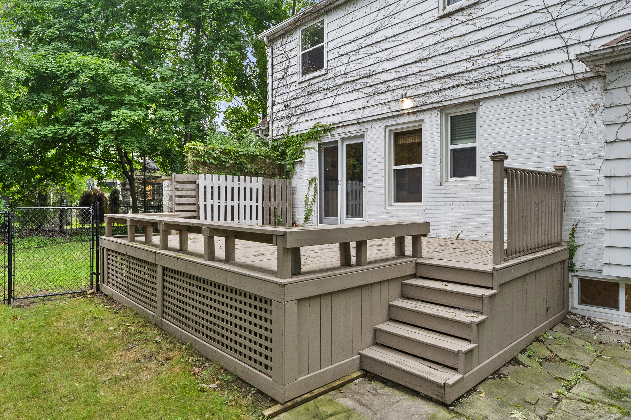 Wooden deck with steps, surrounded by greenery and a white house