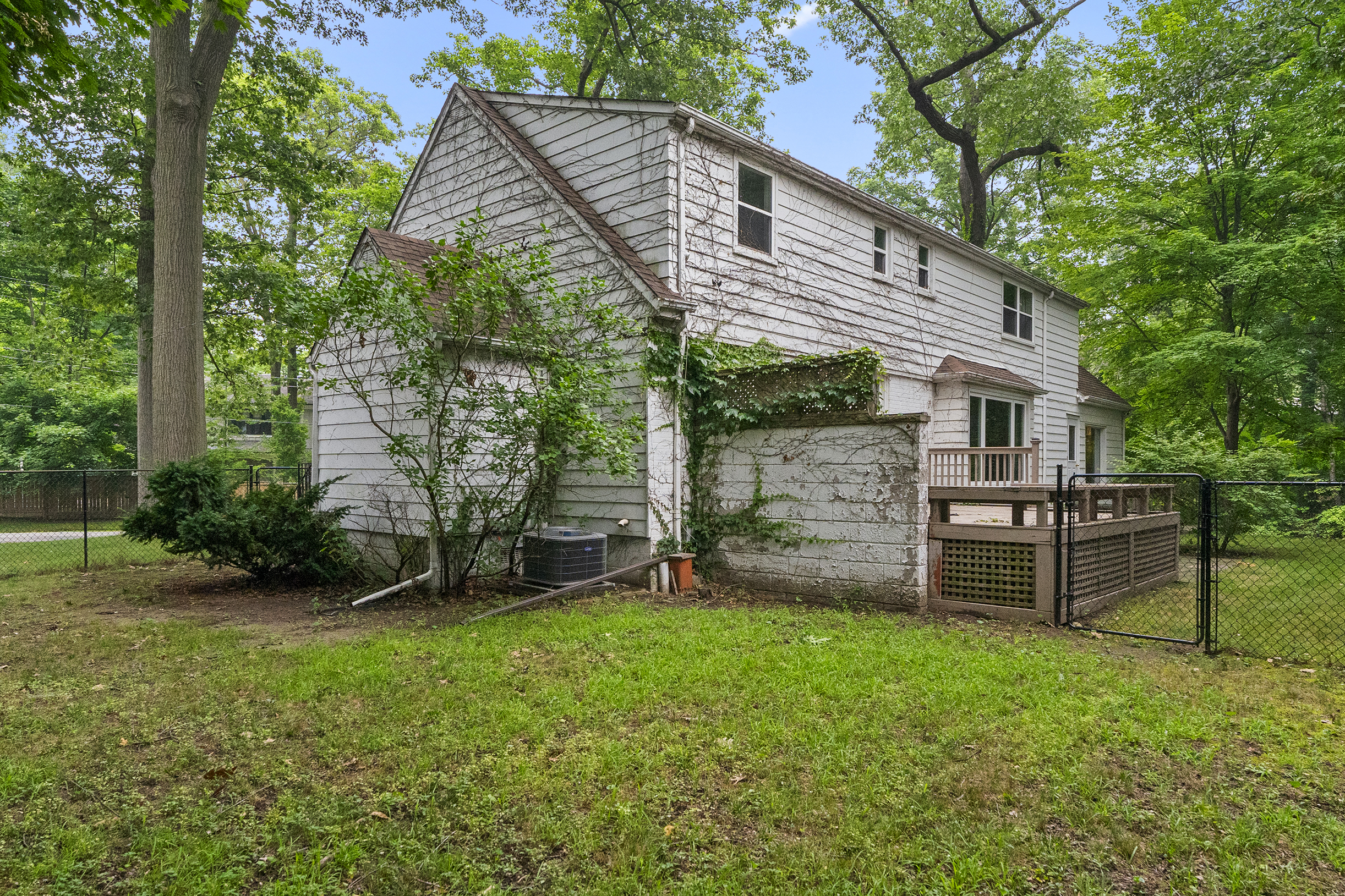 Two-story house with a wooden deck surrounded by trees and grass