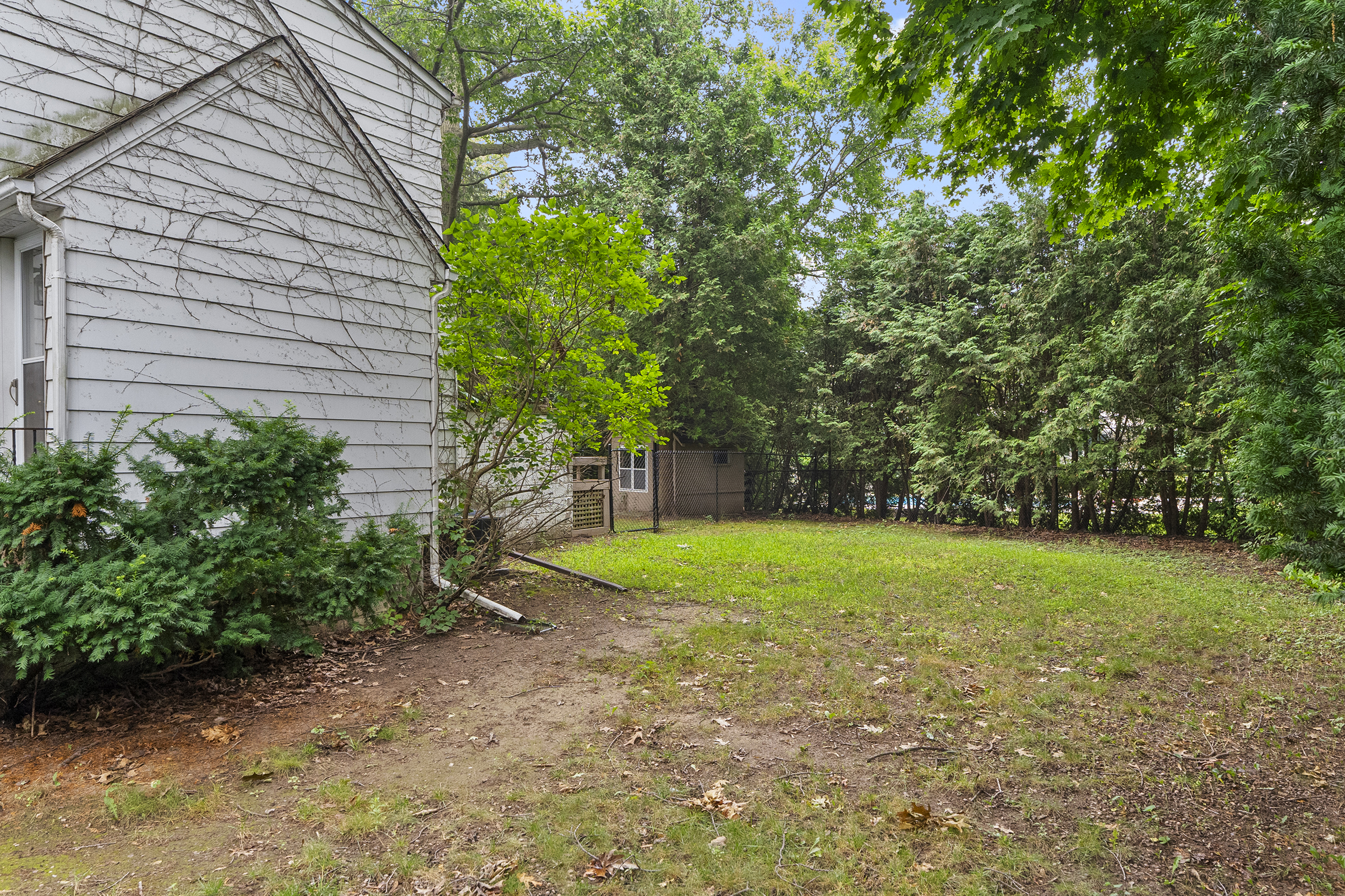 Side yard of a house with green grass and trees in the background