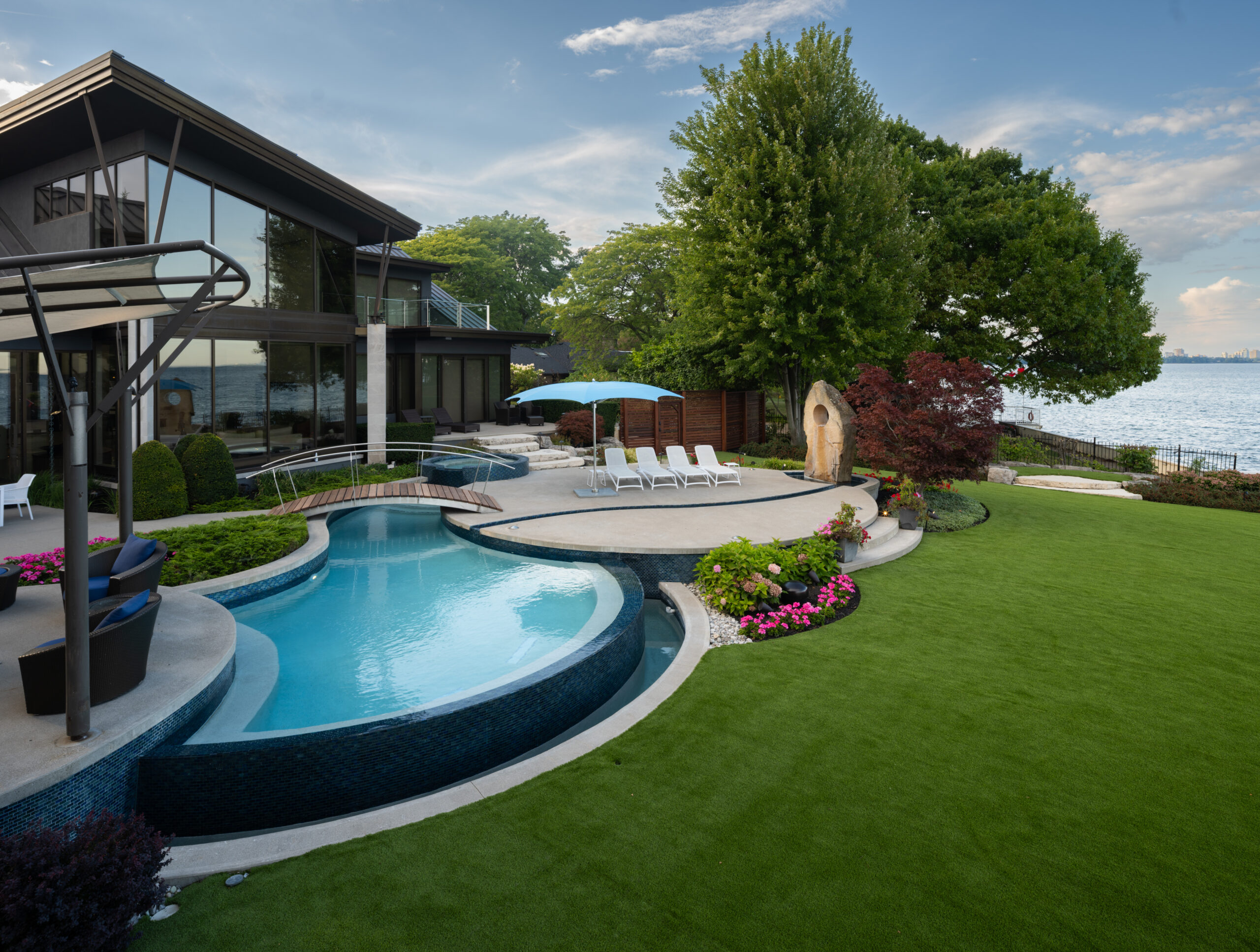 Modern pool area with lush green lawn and patio furniture by the water