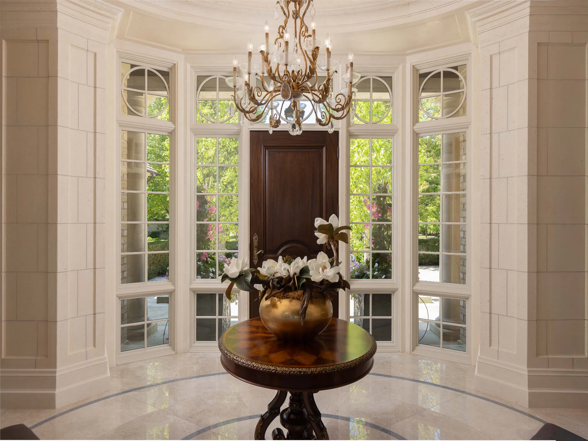 Elegant foyer with chandelier, round table, and large windows.