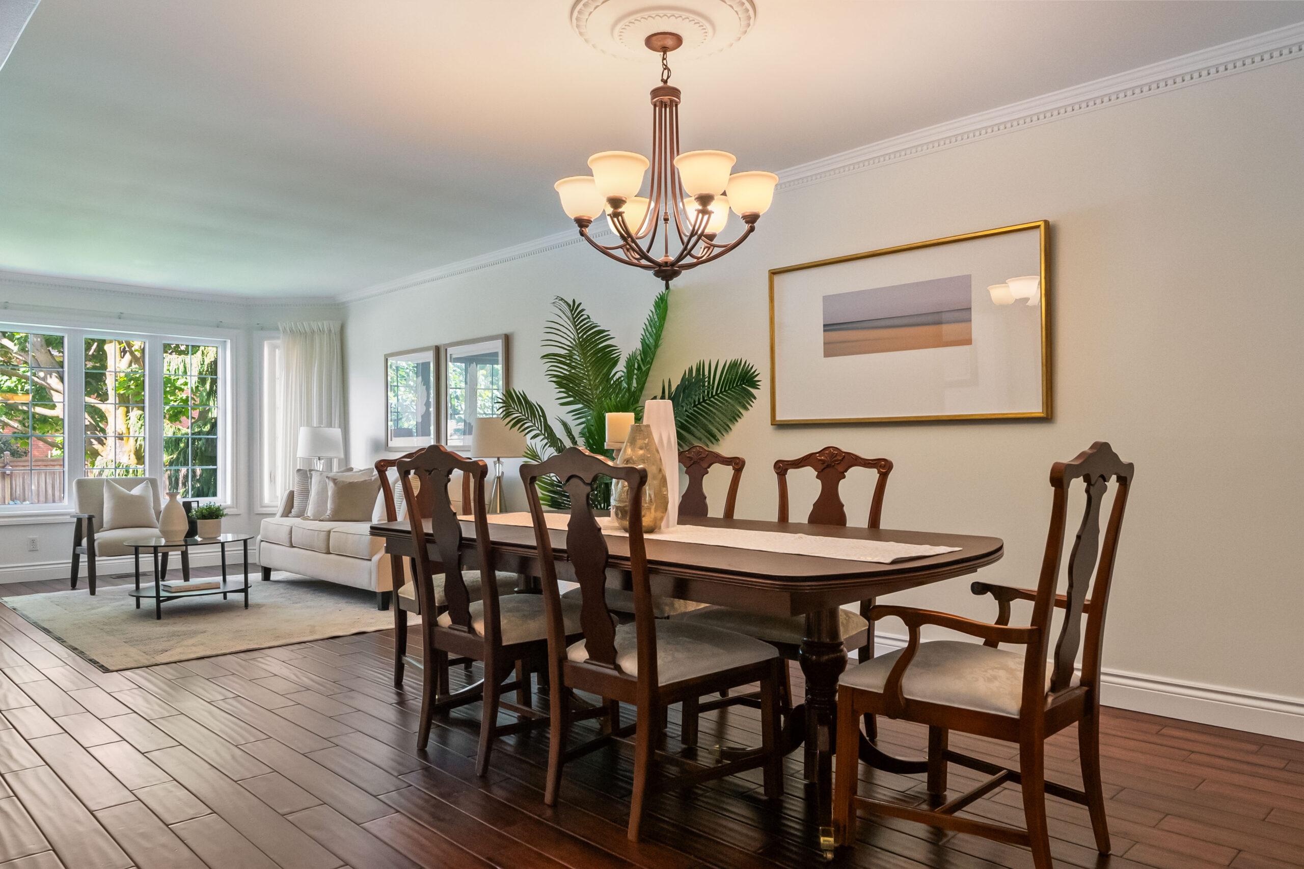 Elegant dining room with wooden table, chairs, and chandelier, featuring natural light.
