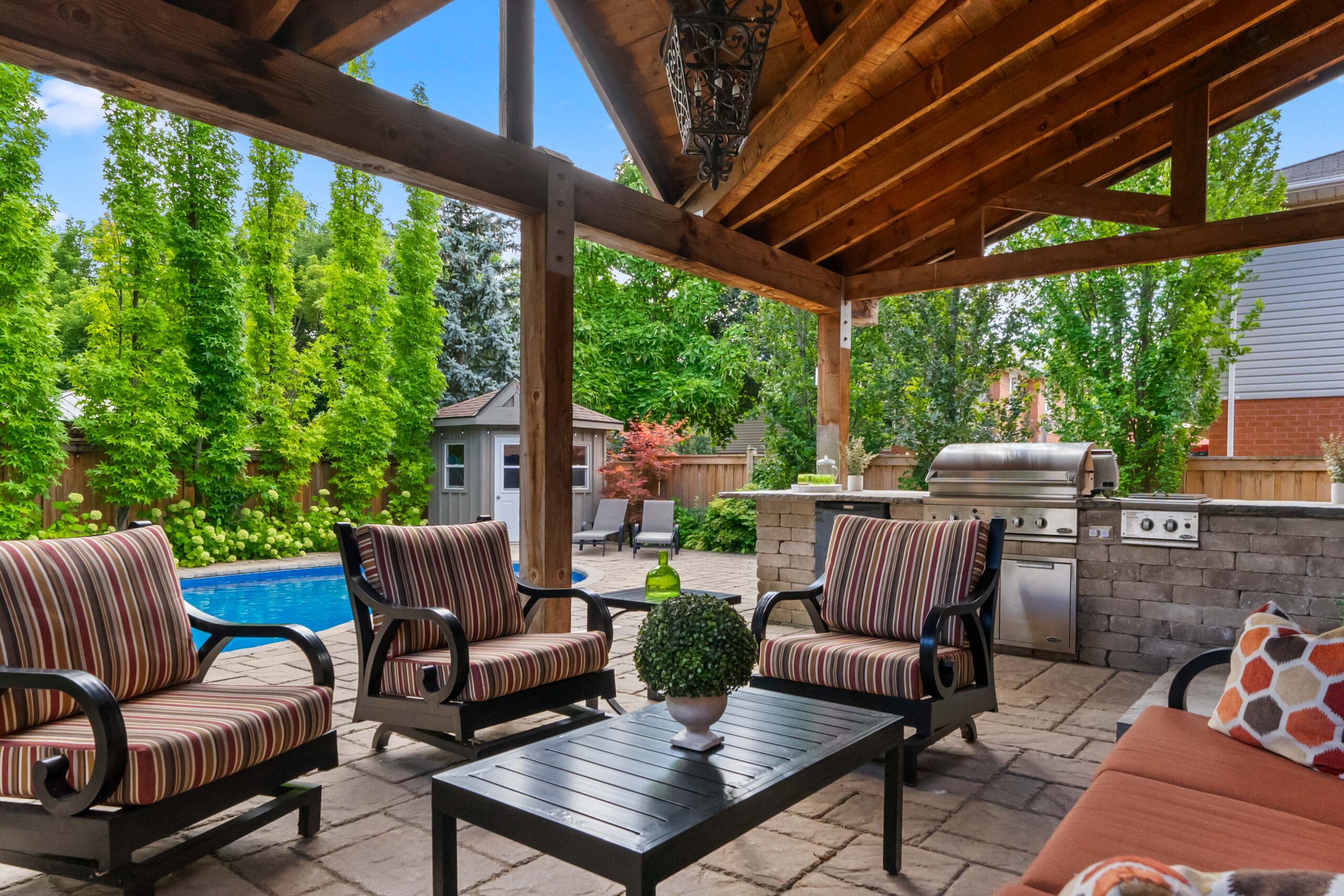Cozy outdoor seating area with a pool and grill under a wooden pergola