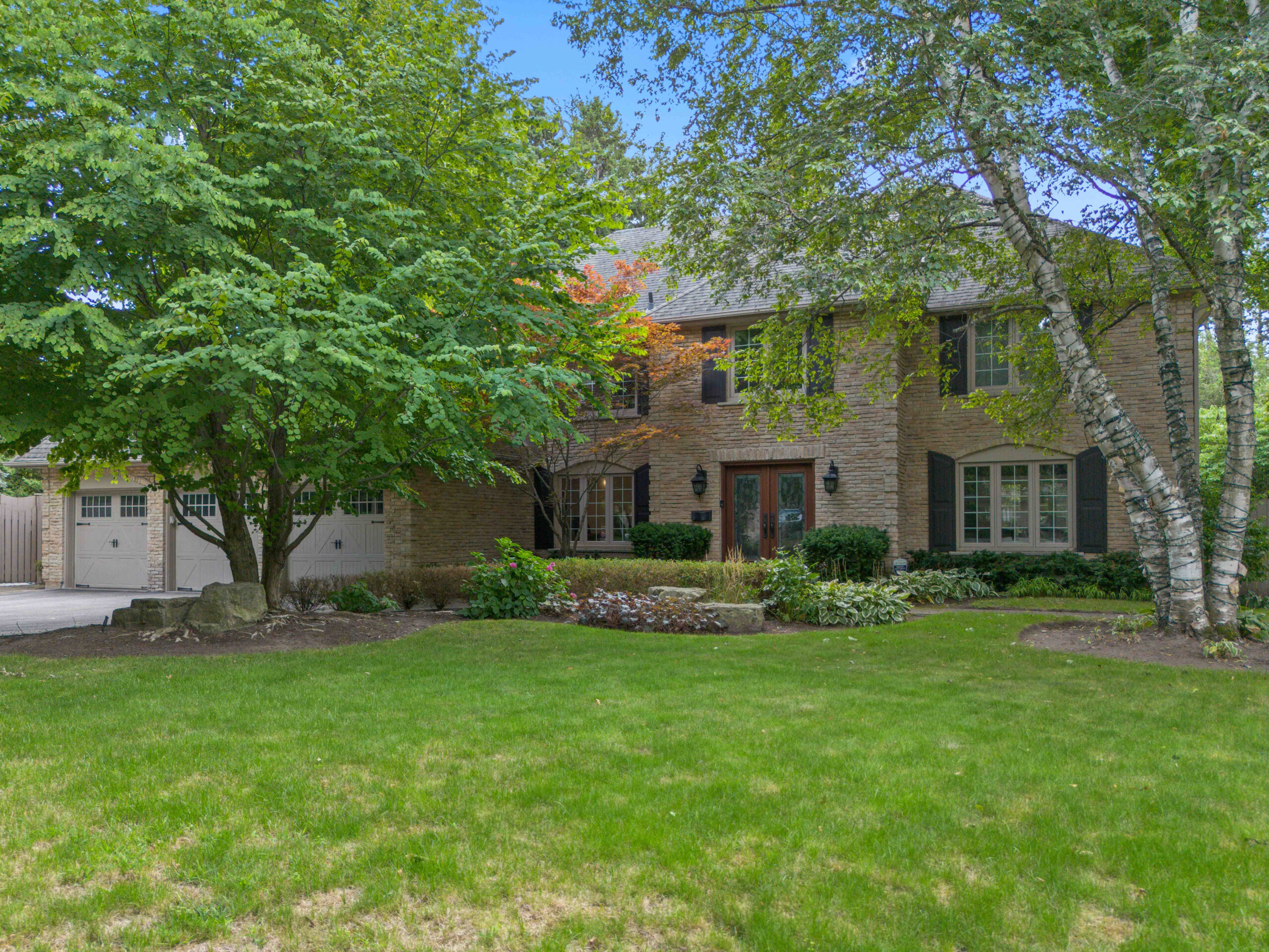 Two-story brick house surrounded by lush greenery and a manicured lawn