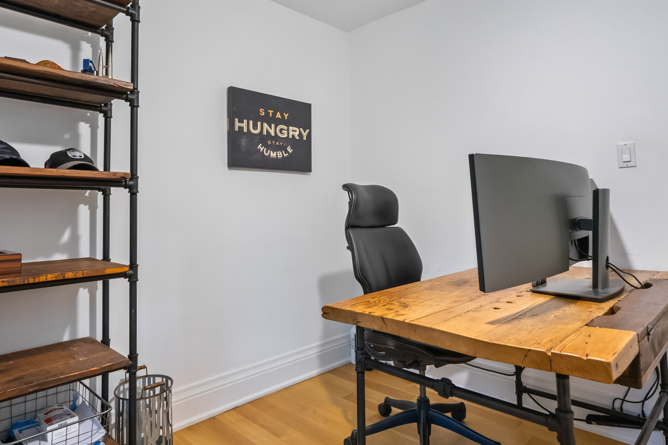 Modern home office with a wooden desk, black chair, and motivational wall art.