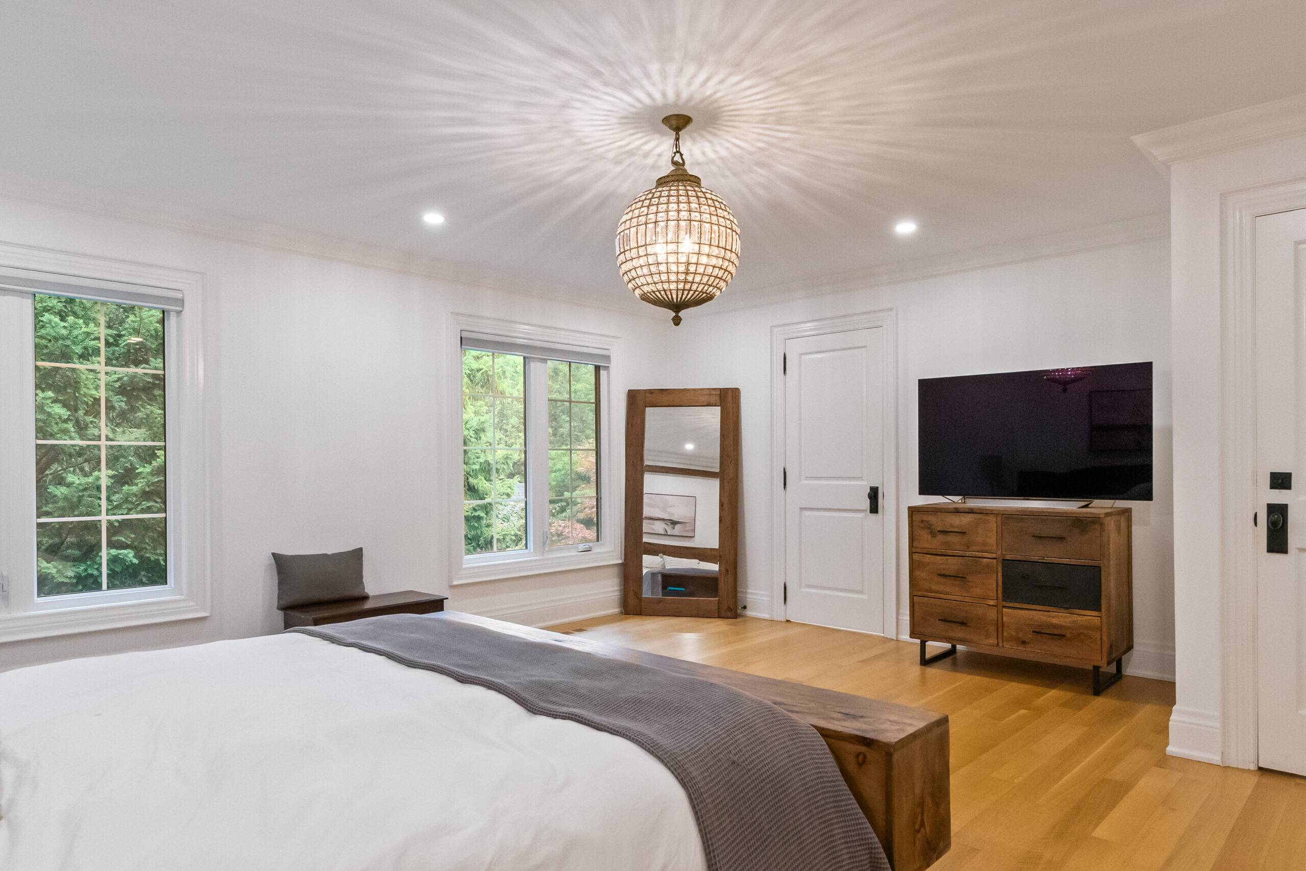 Modern bedroom with a chandelier, wooden furniture, and large windows