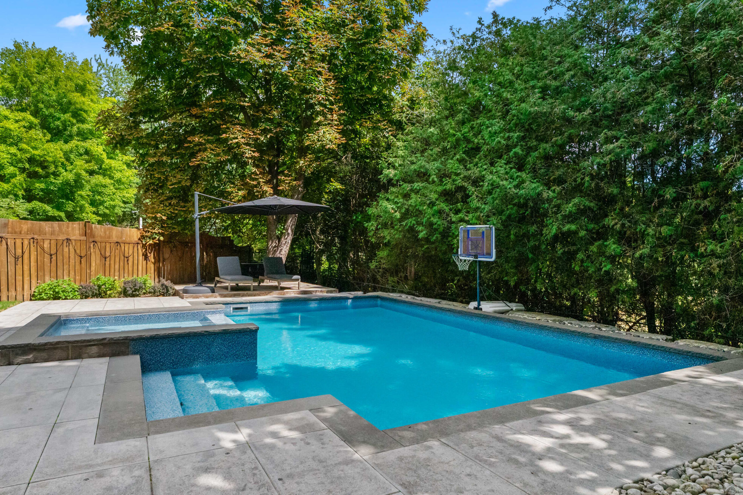 Backyard pool surrounded by greenery and patio furniture
