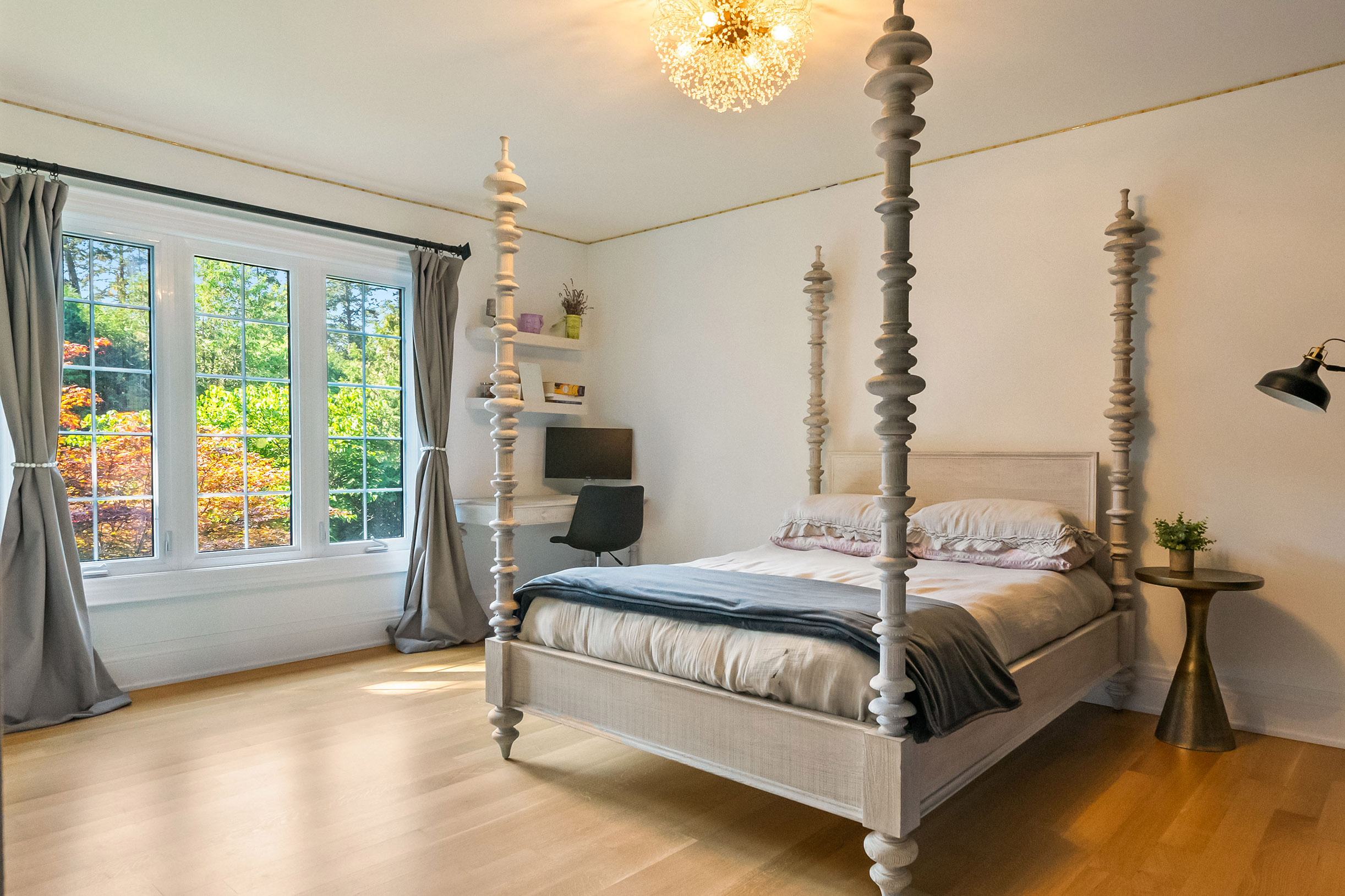 Bright bedroom featuring a four-poster bed, large windows, and wooden flooring