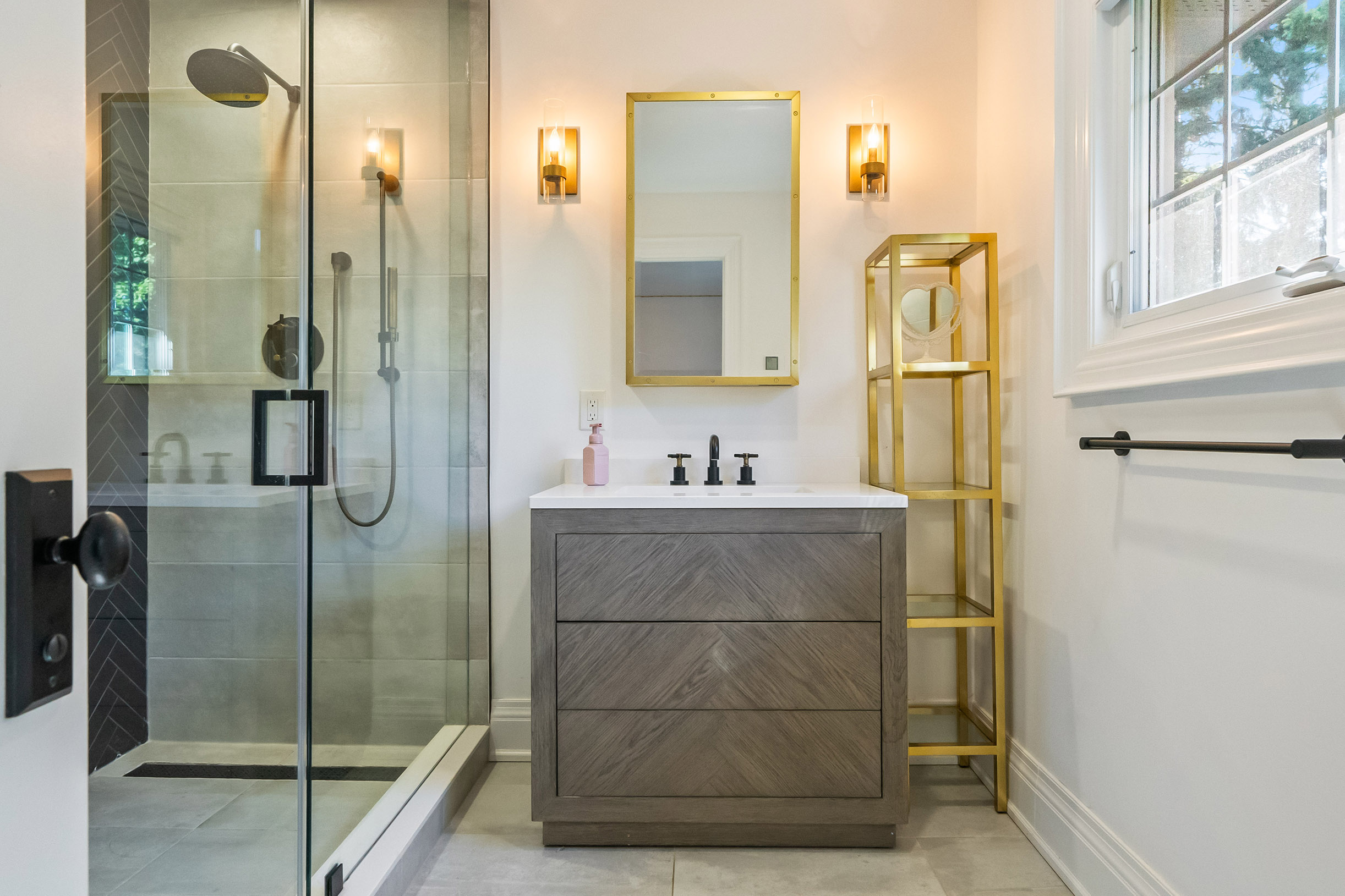 Modern bathroom featuring a glass shower, wooden vanity, and gold accents.