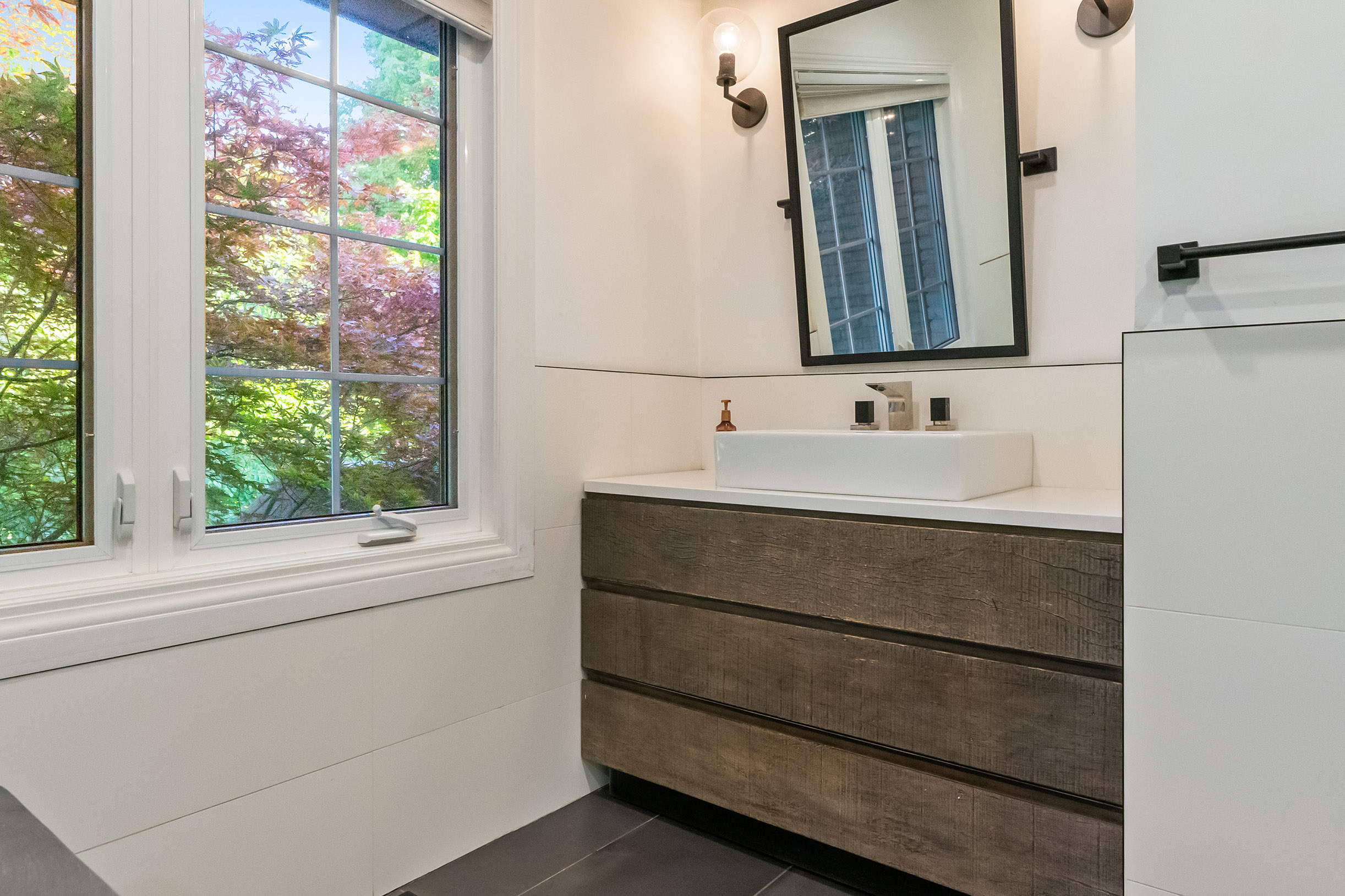 Modern bathroom with wooden vanity, mirror, and large window view.