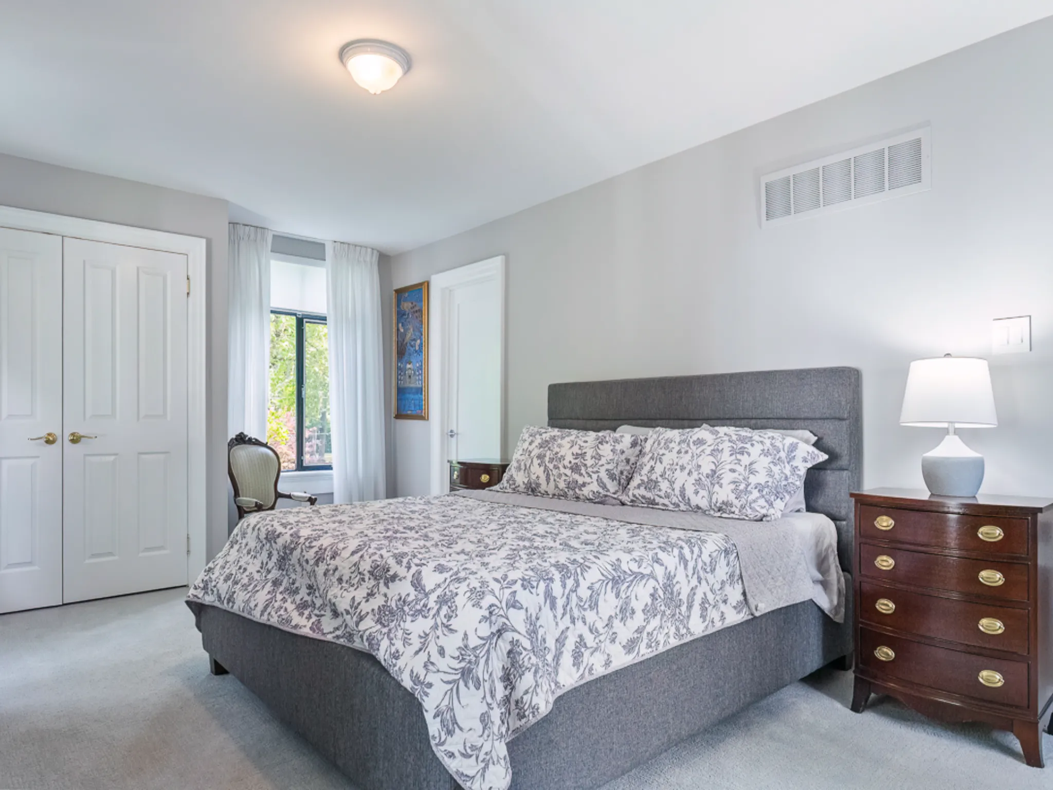 Cozy bedroom with gray bedding, wooden nightstand, and natural light.
