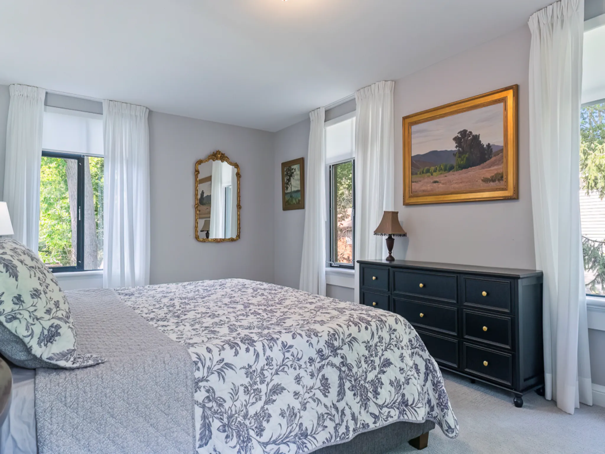 Cozy bedroom with gray bedding, wooden nightstand, and natural light.