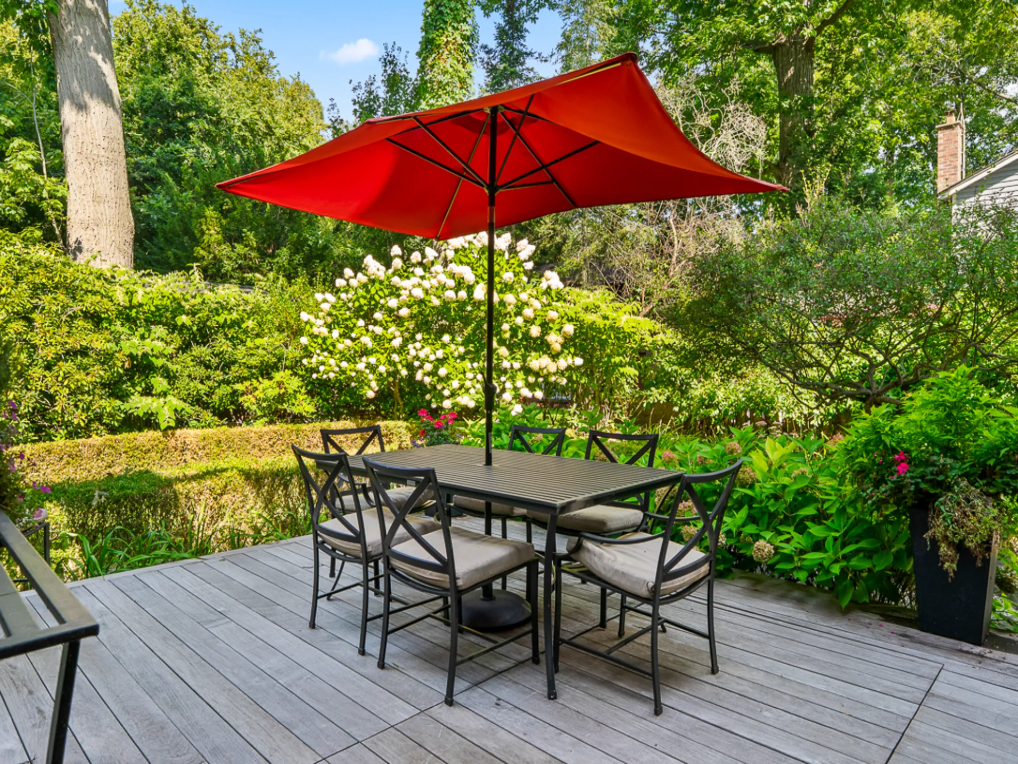 Outdoor dining area with a red umbrella and lush greenery