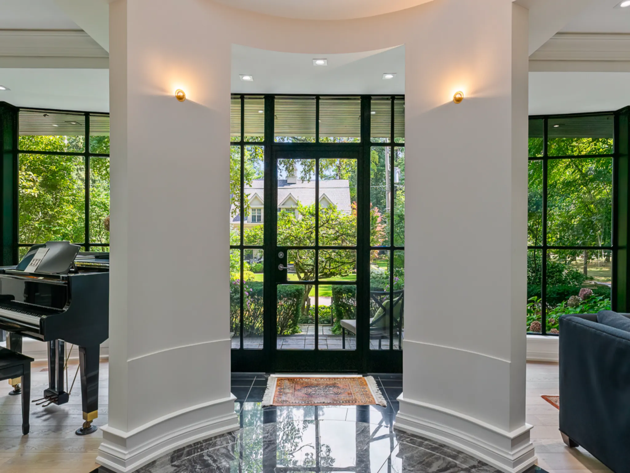 Elegant entryway with large windows and piano, surrounded by greenery