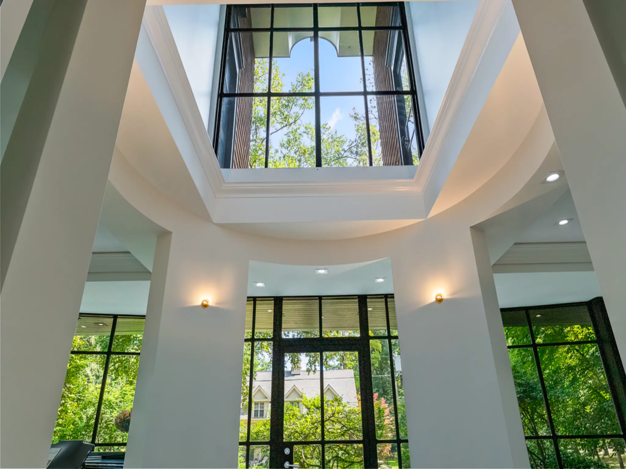 Modern interior with large windows and skylight, surrounded by greenery