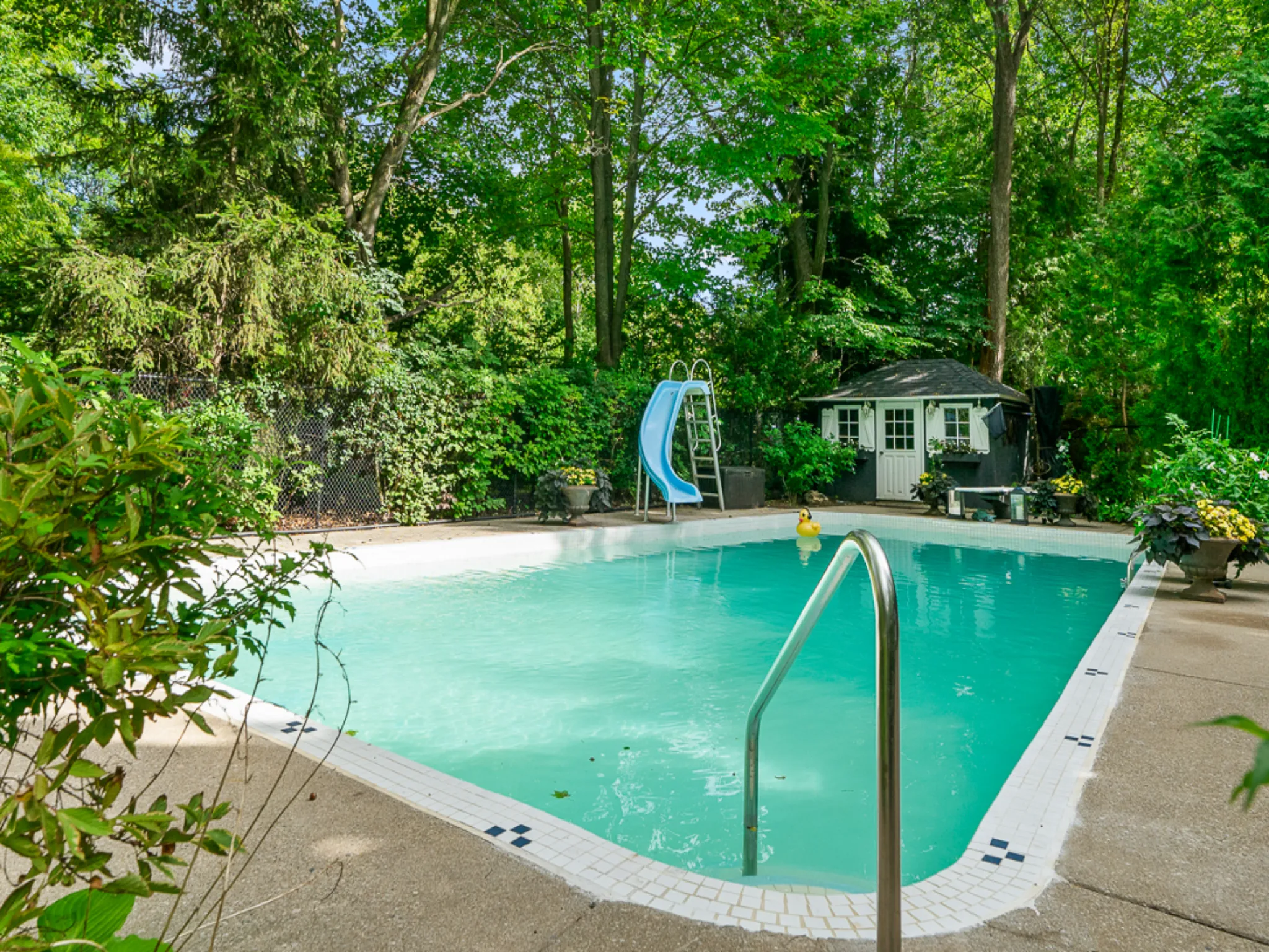 large yard with tall trees and pool with a blue slide