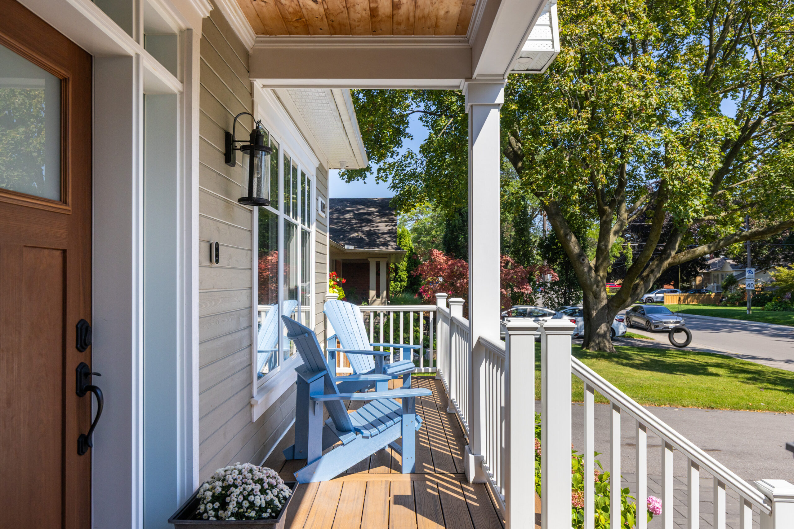 Front porch with blue chairs and white railing, surrounded by greenery