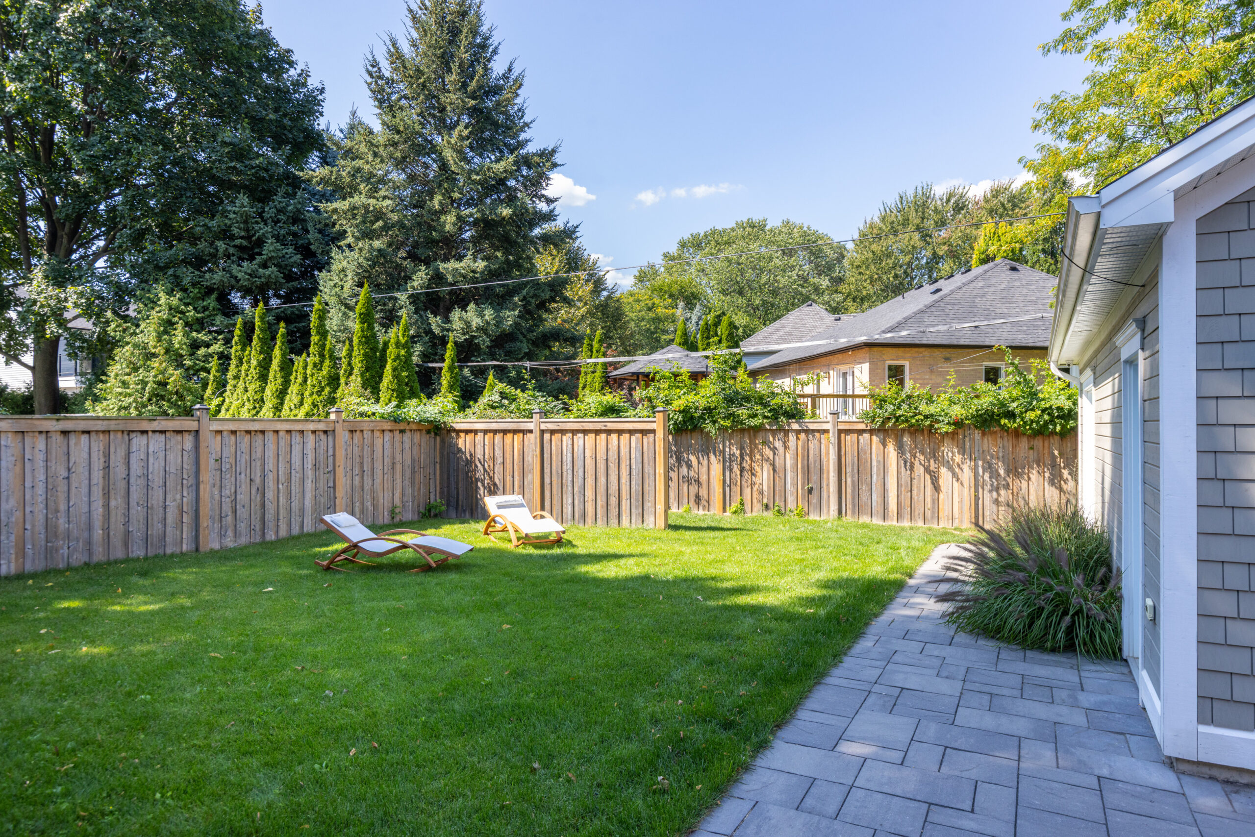 Sunny backyard with green lawn, lounge chairs, and wooden fence