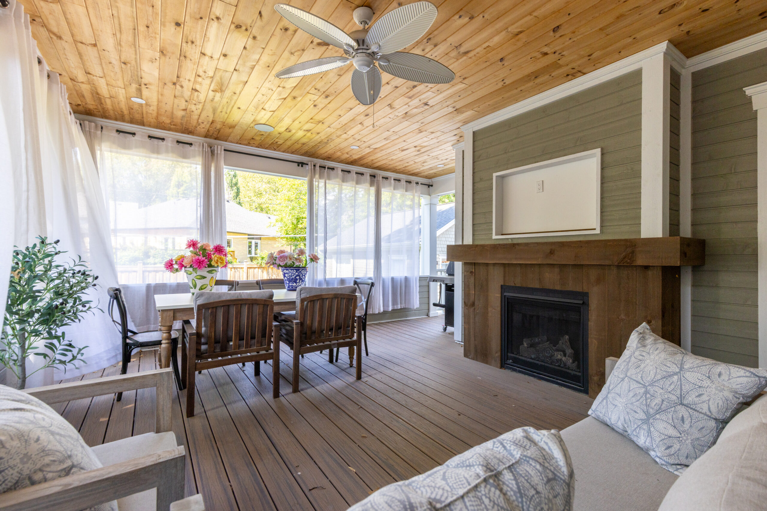 Cozy screened porch with wooden ceiling, dining table, and fireplace