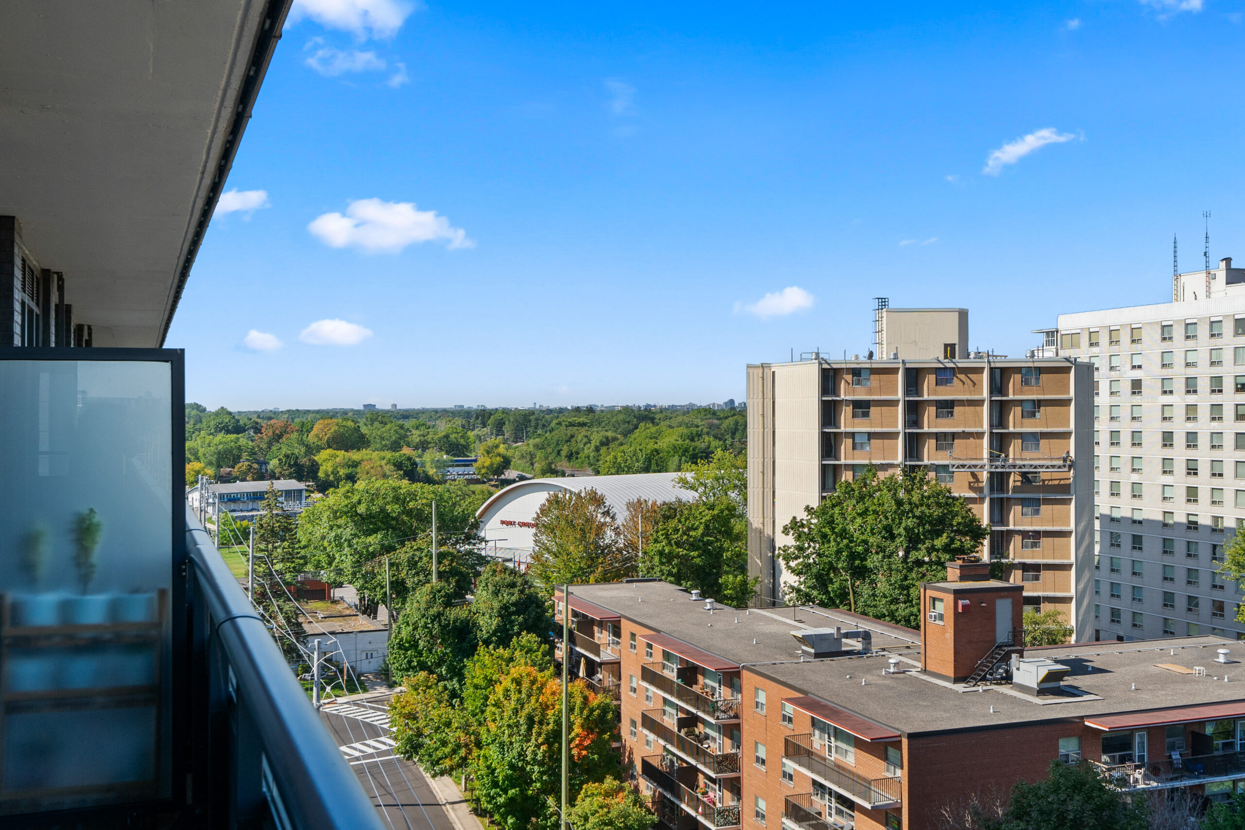 Cityscape view from a balcony with green trees and buildings under a blue sky