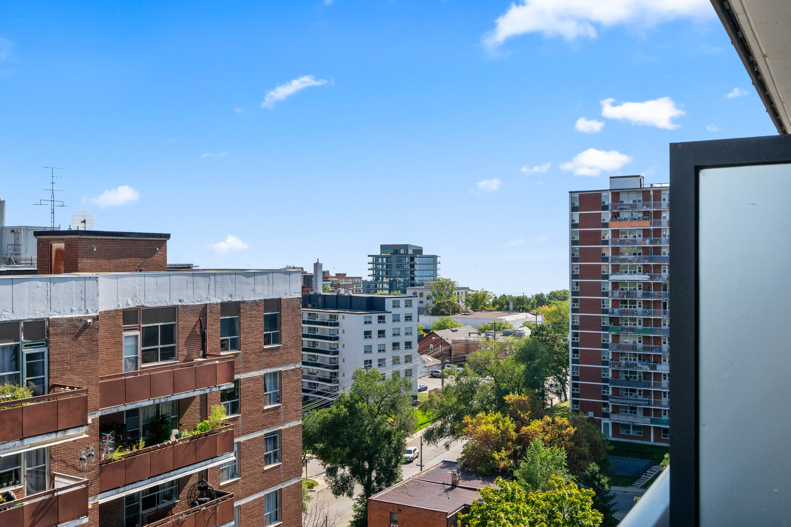 Cityscape view from a balcony featuring buildings and greenery under a blue sky