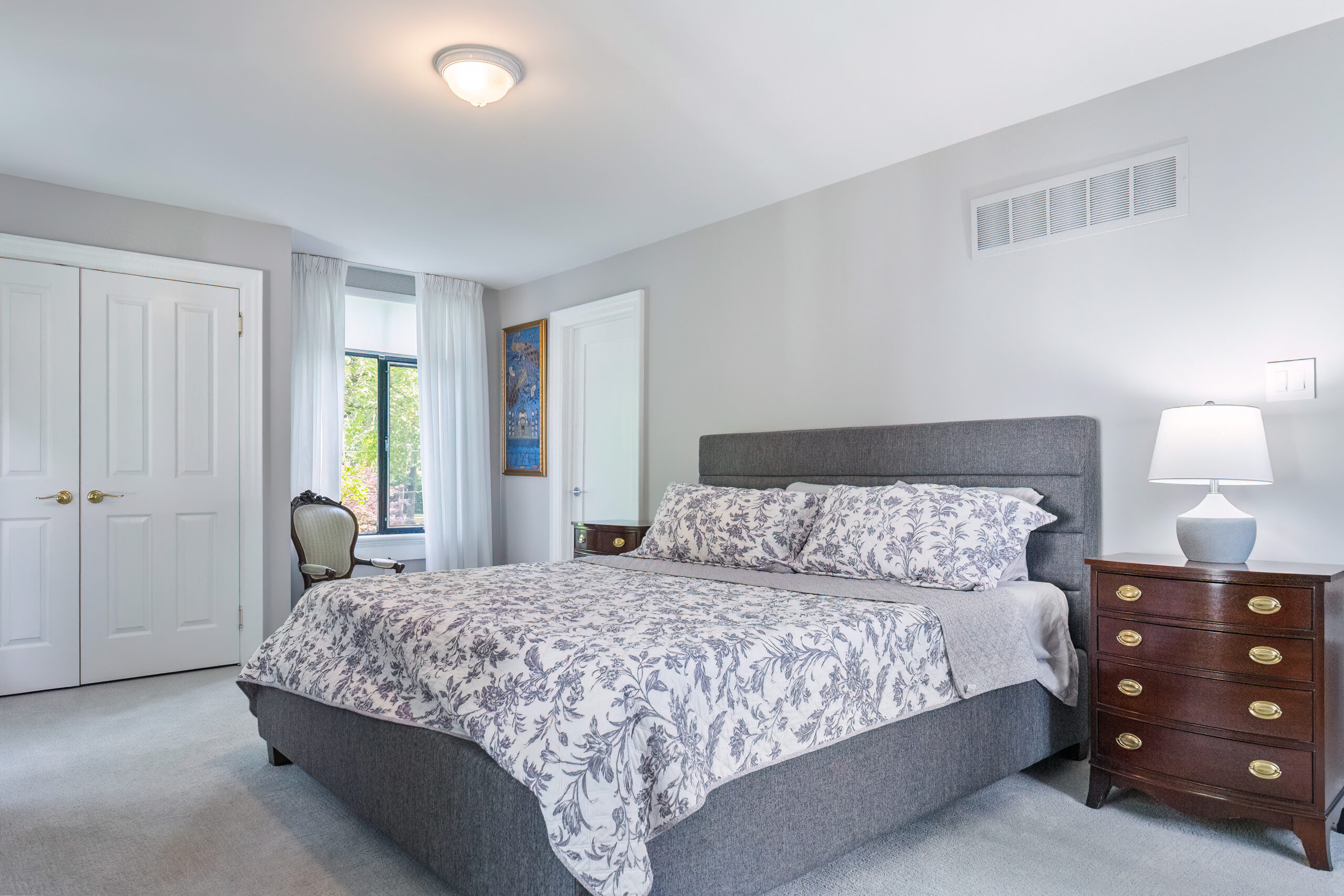 Cozy bedroom with gray bedding, wooden nightstand, and natural light.