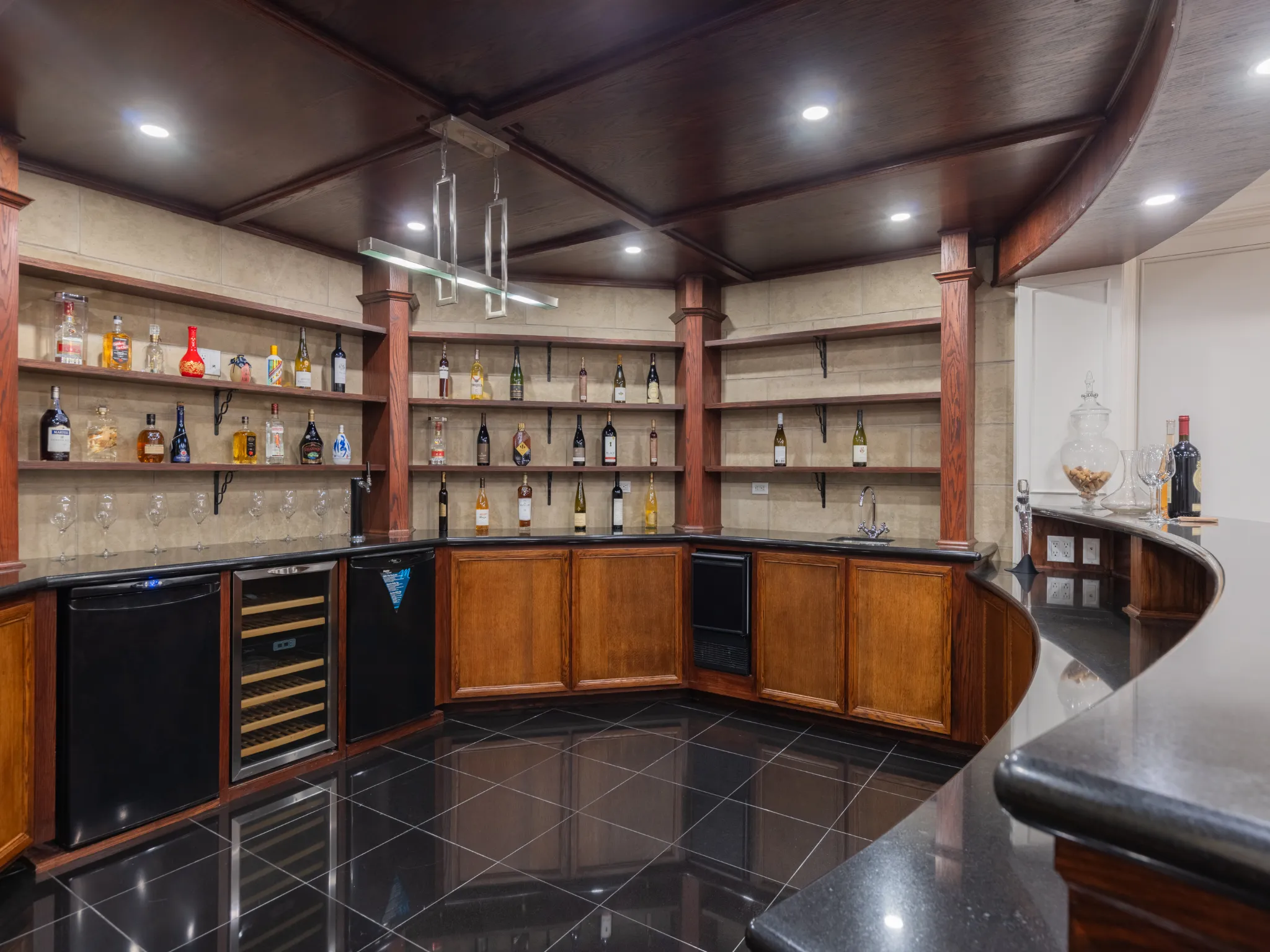lower level wet bar with wood coloured cabinets, open shelves, beverage fridge.