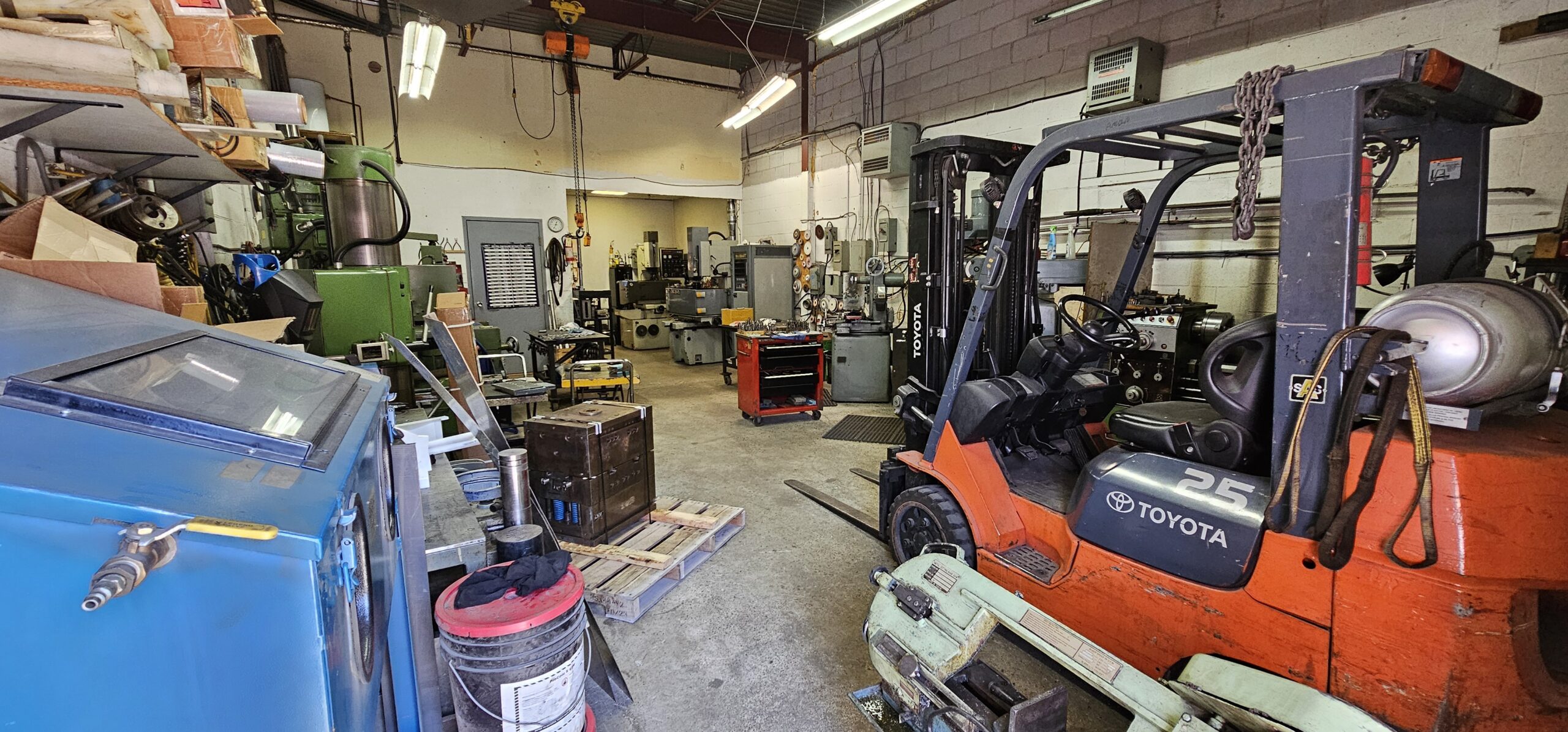 Cluttered workshop with machinery, tools, and a forklift in view