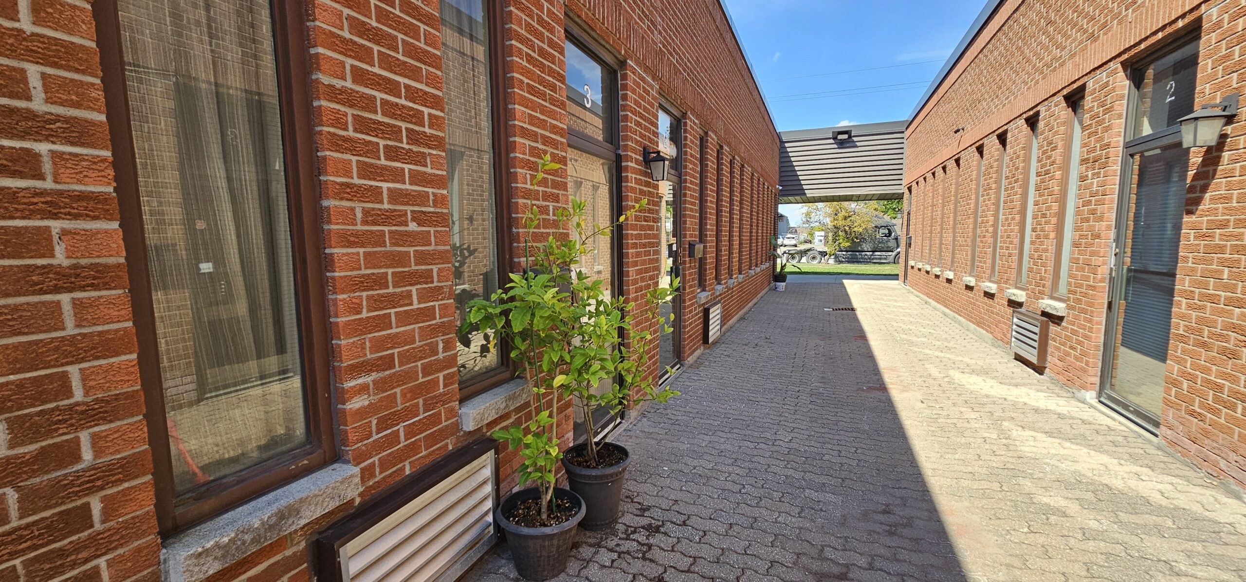 Narrow brick pathway between buildings with potted plants and blue sky