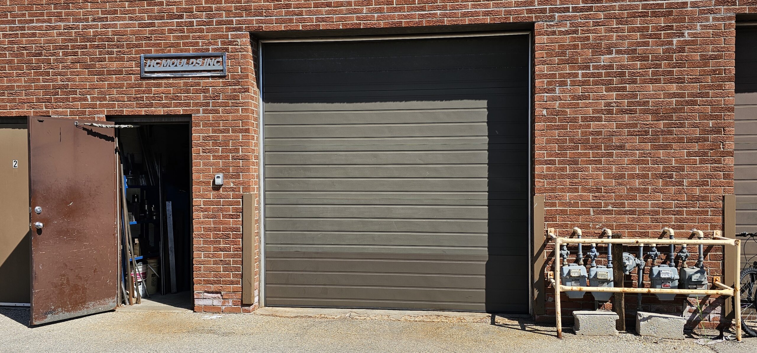 Brown brick building with a large garage door and open side door.
