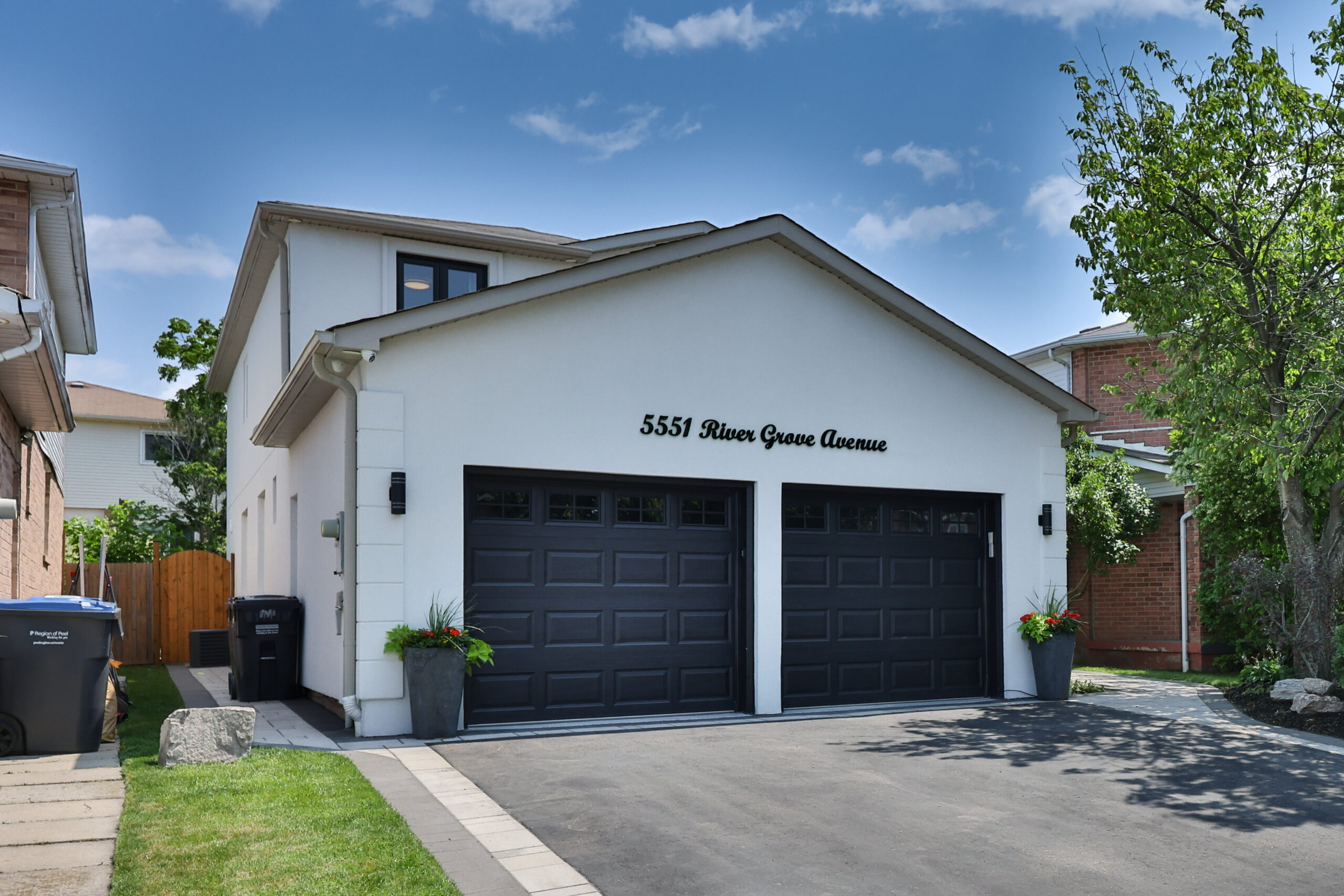 Modern two-car garage with black doors and green plants, blue sky above