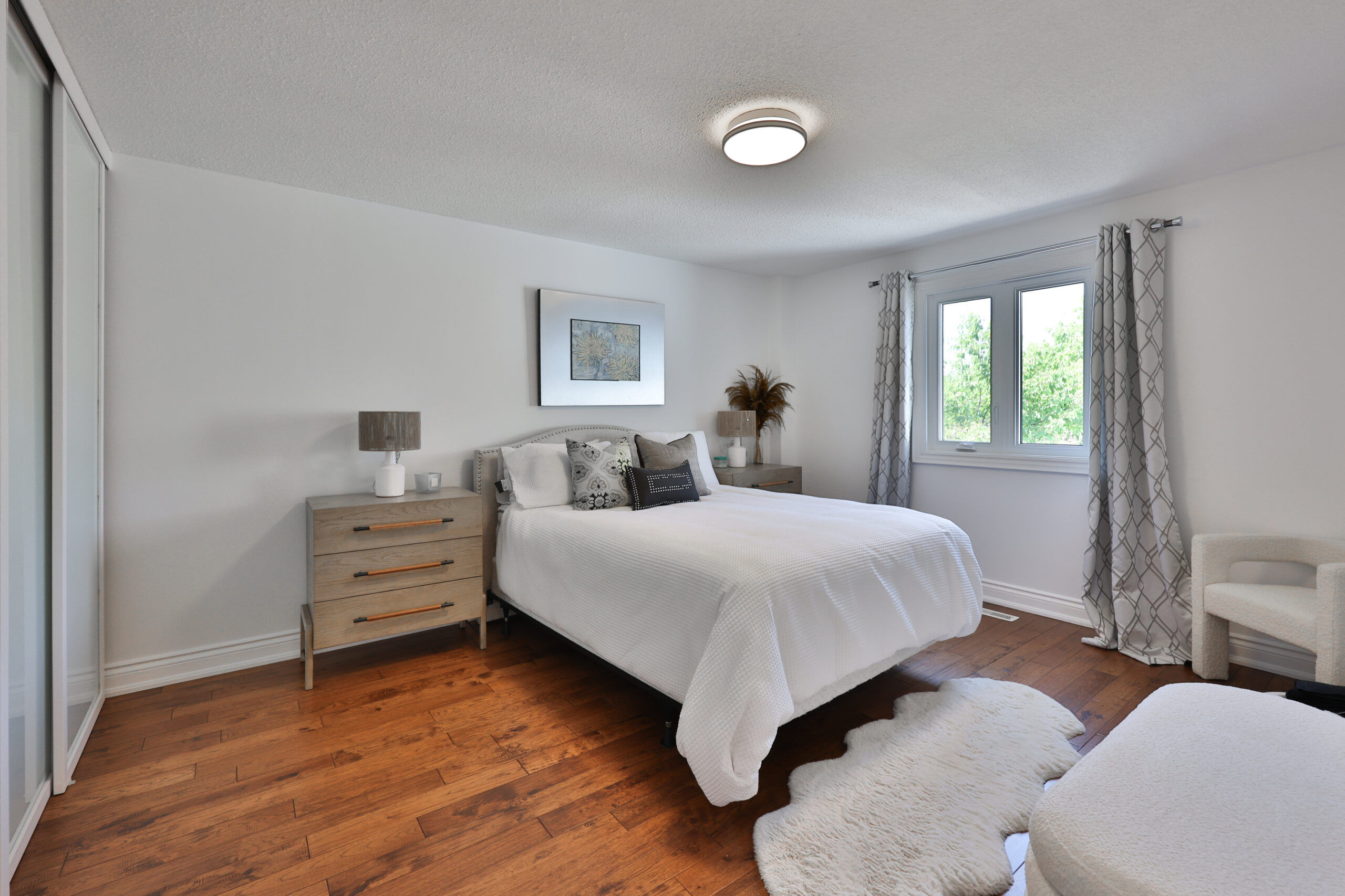 Bright bedroom with a white bed, wooden floor, and large window